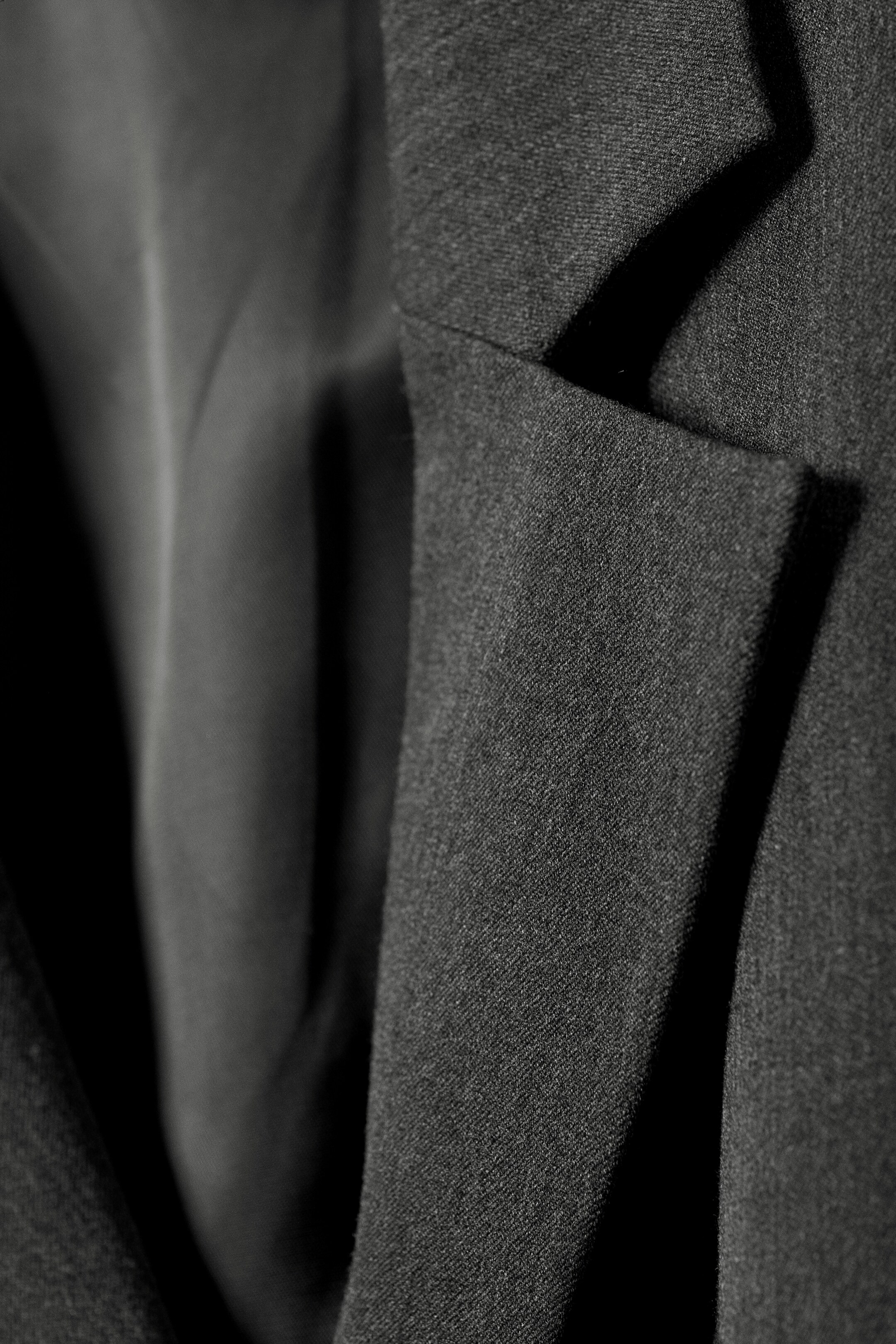 Größeres Bild anzeigen: Ein dunkler Blazer präsentiert seinen strukturierten Außenstoff und ein markantes Kerbrevers. Sein glattes Innenfutter ist sichtbar und schafft einen sanften Kontrast darunter.