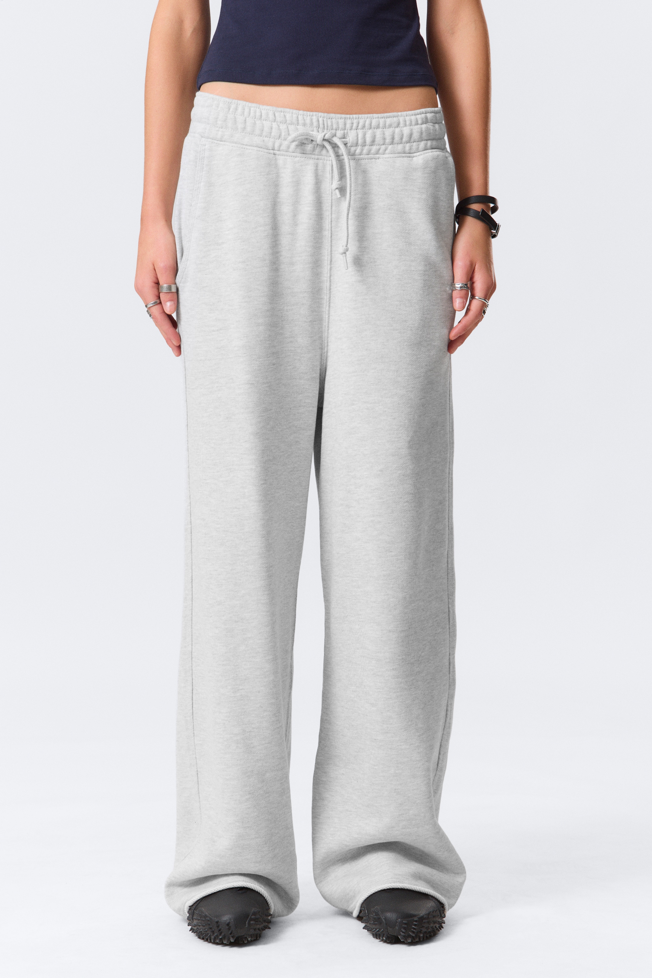 Agrandir l'image: Un pantalon de survêtement gris clair est présenté de face, avec une taille élastique côtelée et un cordon de serrage visible. Le pantalon présente une coupe décontractée et large, avec une longueur qui s'accumule sur les chaussures du porteur.