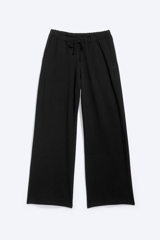 Pantalonii de pijama negri sunt prezentați frontal, afișând o talie elastică cu șnur și buzunare laterale oblice. Aceștia au un croi relaxat, cu o siluetă largă. - 1