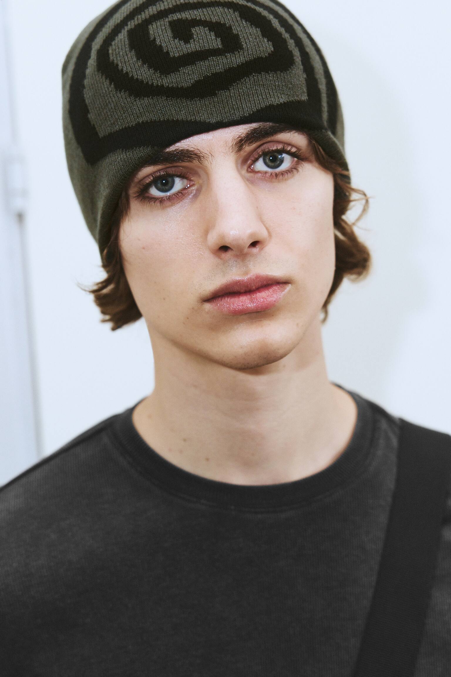 La modelo lleva un gorro de punto ajustado con un estampado grÃ¡fico en negro y verde oliva. El gorro se ajusta pegado a la frente, sin vuelta en el borde, y se combina con una prenda de cuello redondo en gris oscuro. - 1