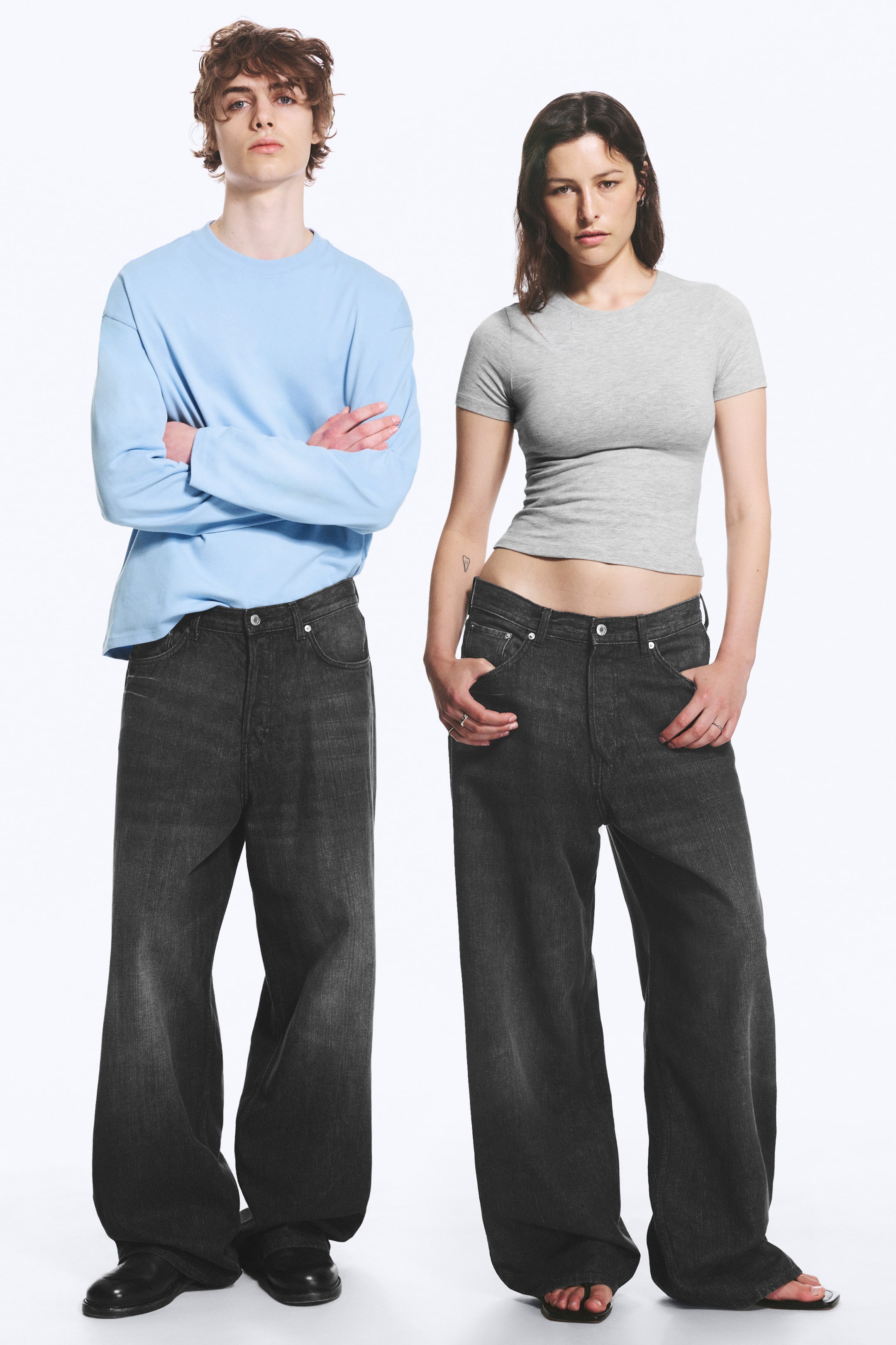 Se større billede: To par sorte wide-leg jeans har en afslappet, løs pasform med en falmet mørk vask. Begge par fremviser en knaplukning og buede forlommer, med de brede ben, der let samler sig ved anklerne, når de præsenteres fra en frontal og let vinklet vinkel.