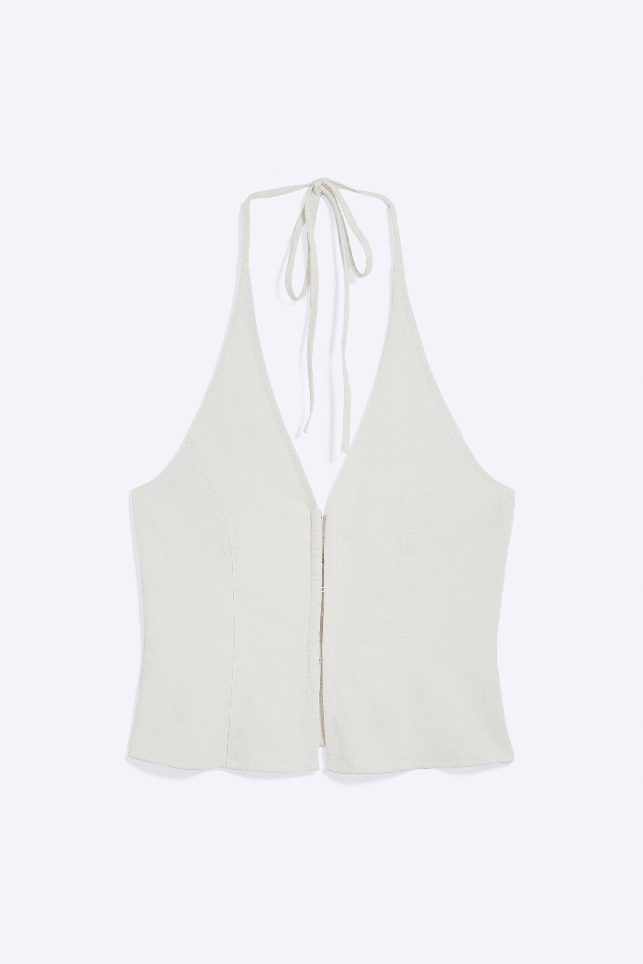 Zobacz większy obraz: Off-biały top z wiązaniem na szyi prezentuje swój przód, charakteryzując się głębokim dekoltem w kształcie litery V oraz cienkimi ramiączkami wiązanymi z tyłu szyi. Zapięcie z przodu na haftki oraz pionowe szwy modelują jego gorset.