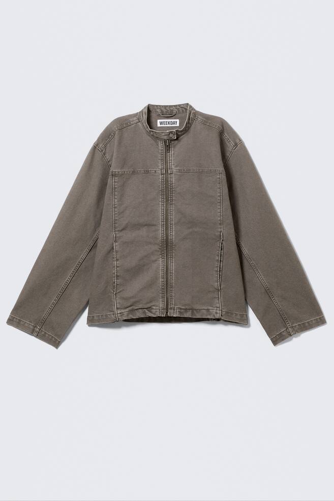 A dark-taupe jacket is shown front-on, featuring a band collar with a snap-button closure and a visible 'WEEKDAY' label. It is designed with a full-length front zip, two side-entry pockets, prominent horizontal seams across the chest, vertical seams down the front, and long sleeves with plain cuffs. - 1