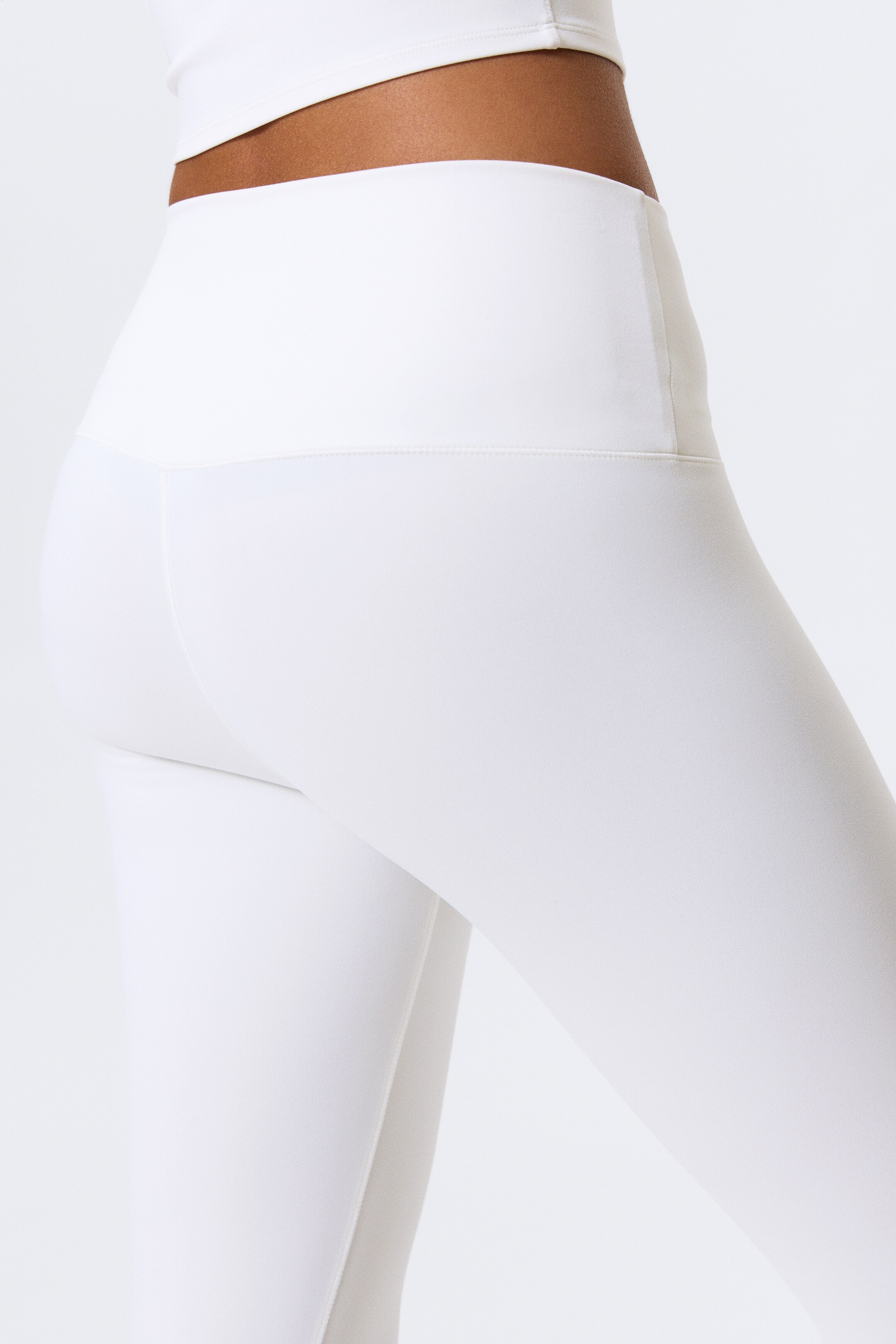 Agrandir l'image: Des leggings blancs taille haute sont présentés sous un angle arrière, mettant en valeur leur design ajusté. Ils présentent une large ceinture lisse et une couture arrière profilée située sous la ceinture.