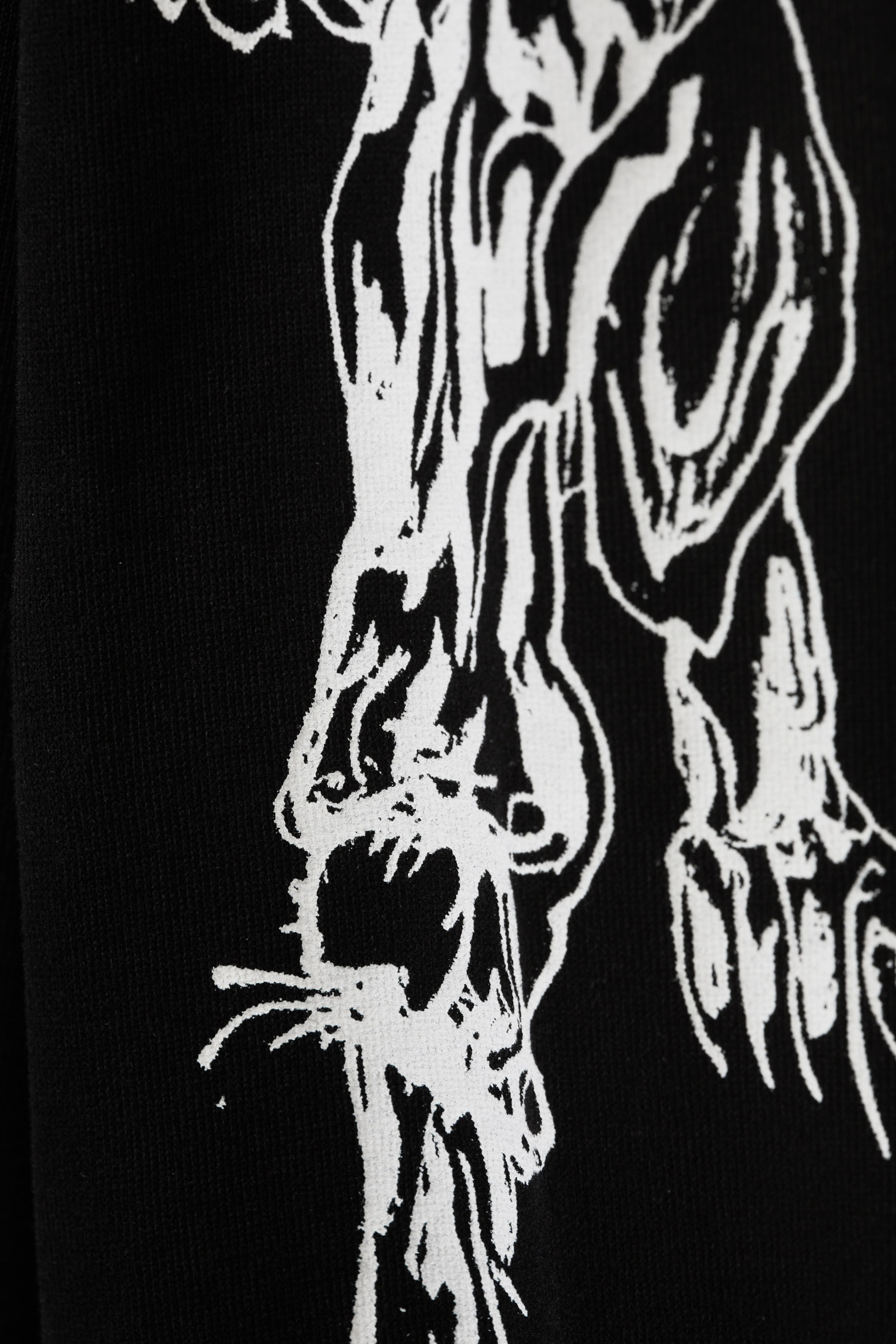 Agrandir l'image: Un T-shirt noir à manches longues affiche une grande impression graphique blanche et complexe sur son tissu en jersey. Le graphique représente des formes squelettiques ou animalistes stylisées et abstraites.
