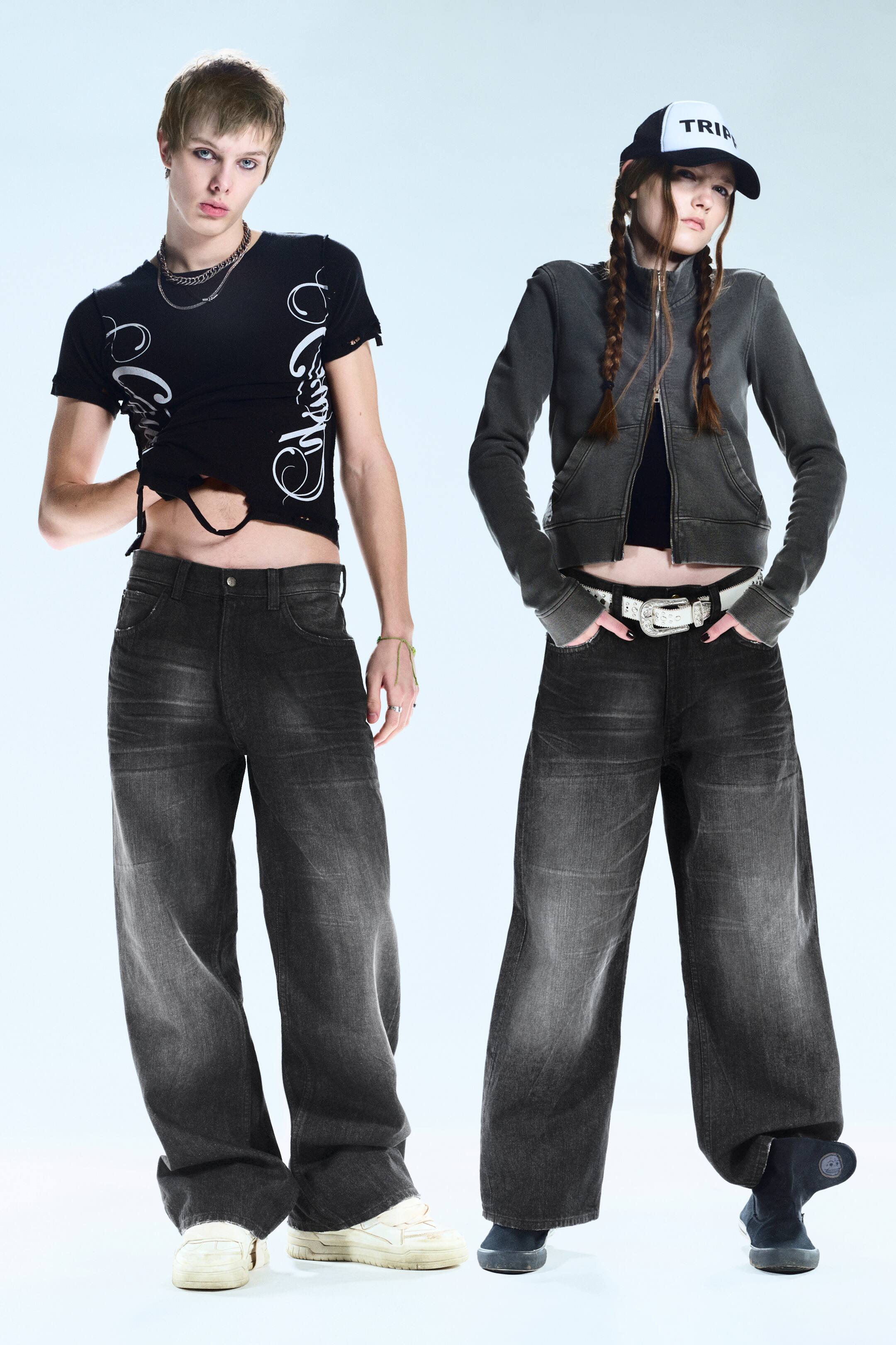 Agrandir l'image: Les jeans en denim à jambes larges présentent un délavage gris foncé, décoloré avec des zones plus claires sur les cuisses et les genoux, offrant une coupe décontractée et ample. Ils sont conçus avec une taille haute, une braguette visible avec bouton et fermeture éclair, et des poches avant, s'étendant sur toute la longueur jusqu'à former un léger amas autour des chevilles.