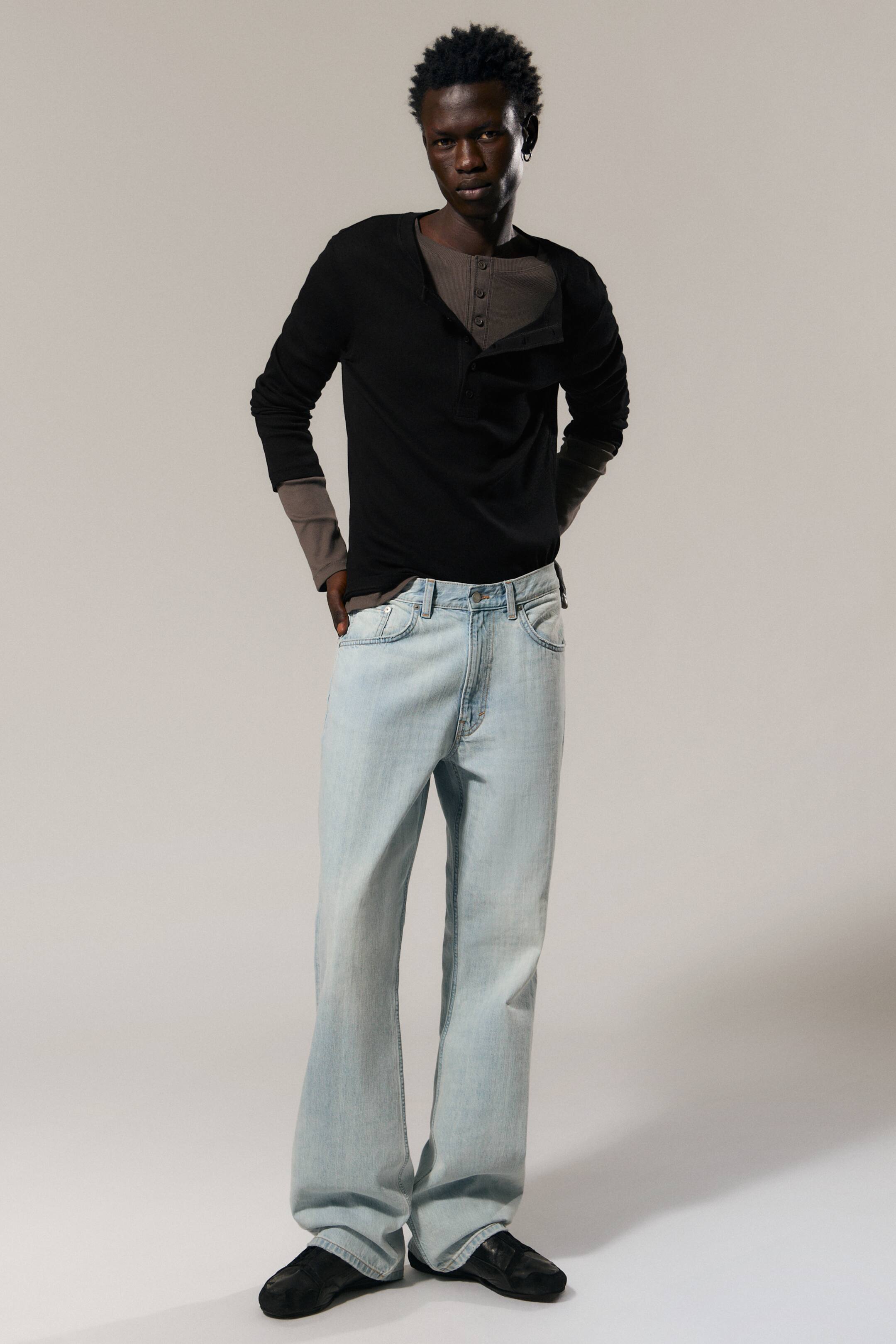 Vezi imaginea mai mare: Blugii din denim cu spălare deschisă prezintă o croială relaxată, cu picior drept, prezentată din față. Aceștia afișează un stil cu cinci buzunare, găici pentru curea și închidere cu nasture și fermoar, cu tivul sprijinindu-se pe pantofi negri.