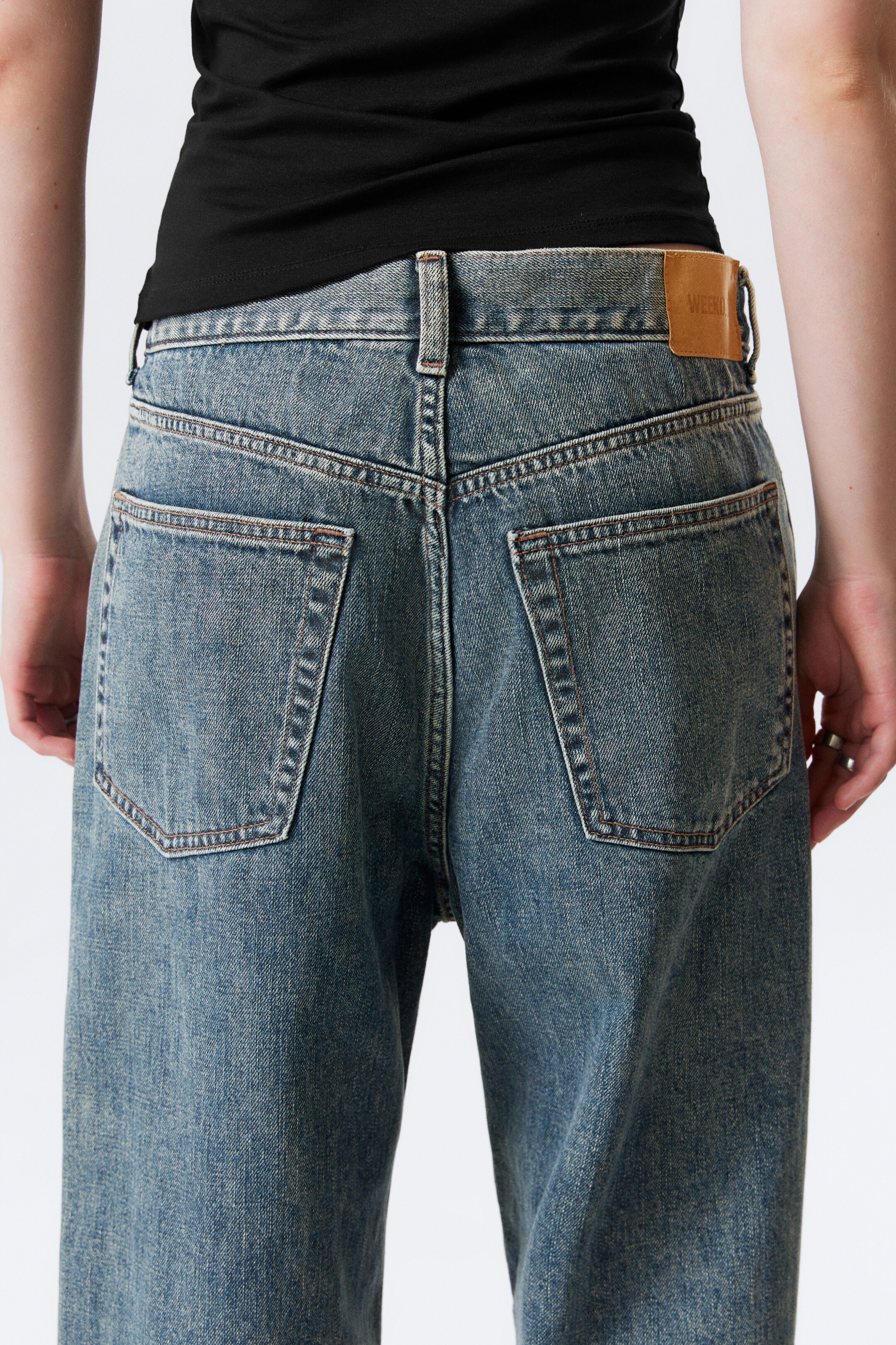 Größeres Bild anzeigen: Eine mittelblaue Jeans wird von hinten gesehen, zeigt eine entspannte Passform und eine subtil verblasste Waschung. Zu den Hauptmerkmalen gehören eine V-förmige Rückenpasse, zwei große aufgesetzte Taschen und ein braunes Leder-Brand-Patch auf der rechten Seite des Bunds.