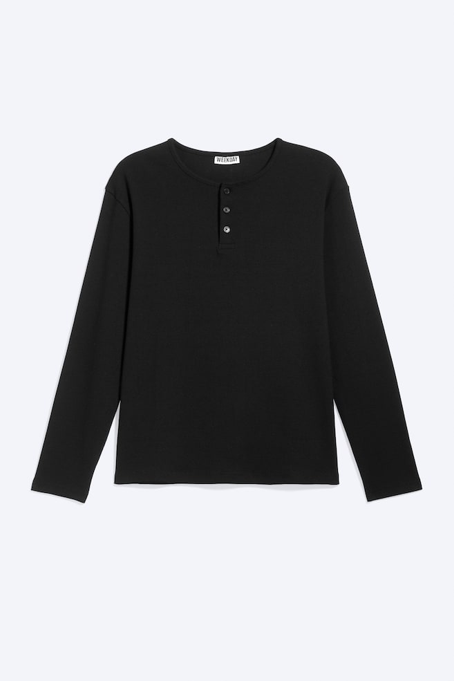 Ein schwarzes Langarm-Henley-Shirt ist nach vorne gerichtet und zeichnet sich durch einen strukturierten Stoff, einen runden Halsausschnitt und eine Dreiknopfleiste mit dunklen Knöpfen aus. Ein "WEEKDAY"-Label ist am Nacken sichtbar. - 1