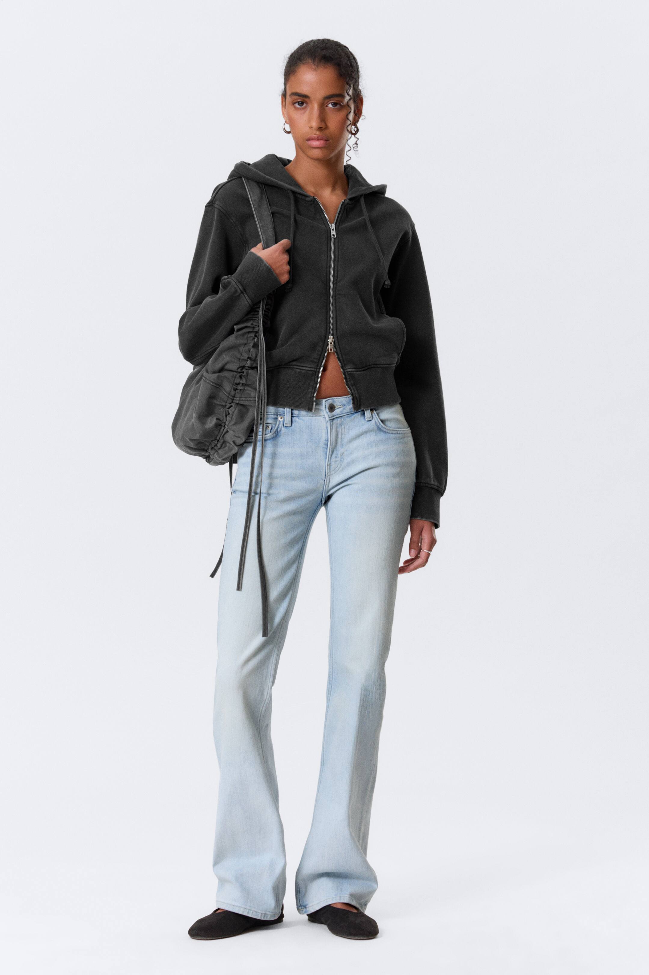 Agrandir l'image: Un sweat à capuche zippé intégral gris foncé délavé est présenté de face, avec une longueur raccourcie, une capuche et une fermeture éclair frontale de couleur argentée. Il dispose de deux poches avant, de poignets côtelés et d'un ourlet côtelé, le tout dans une coupe décontractée.