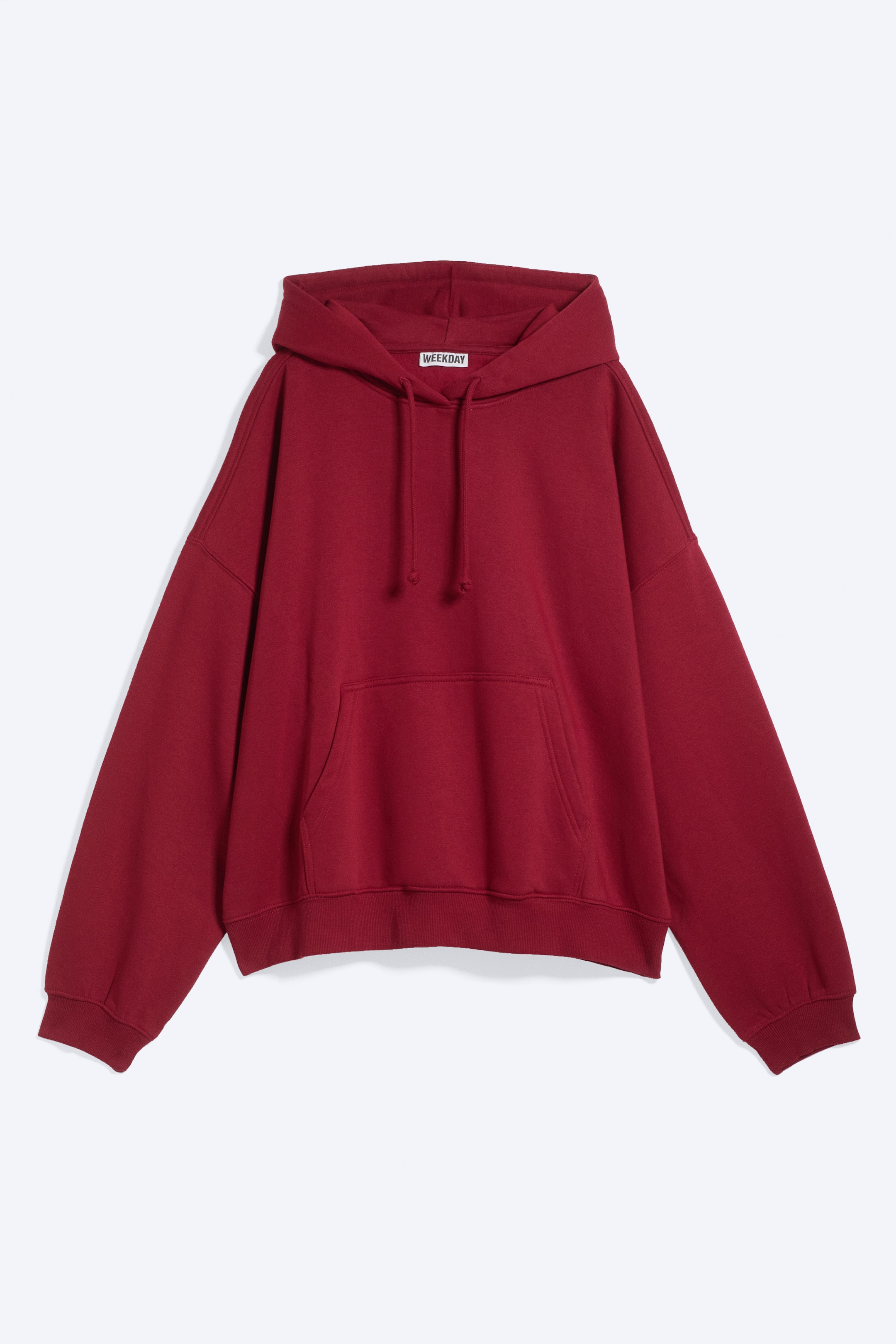Ver imagen más grande: Una sudadera con capucha extragrande de color rojo intenso aparece de frente, con capucha y cordones a juego, un gran bolsillo tipo canguro y puños y bajo acanalados. Se ve una etiqueta de la marca "WEEKDAY" en el interior del escote.