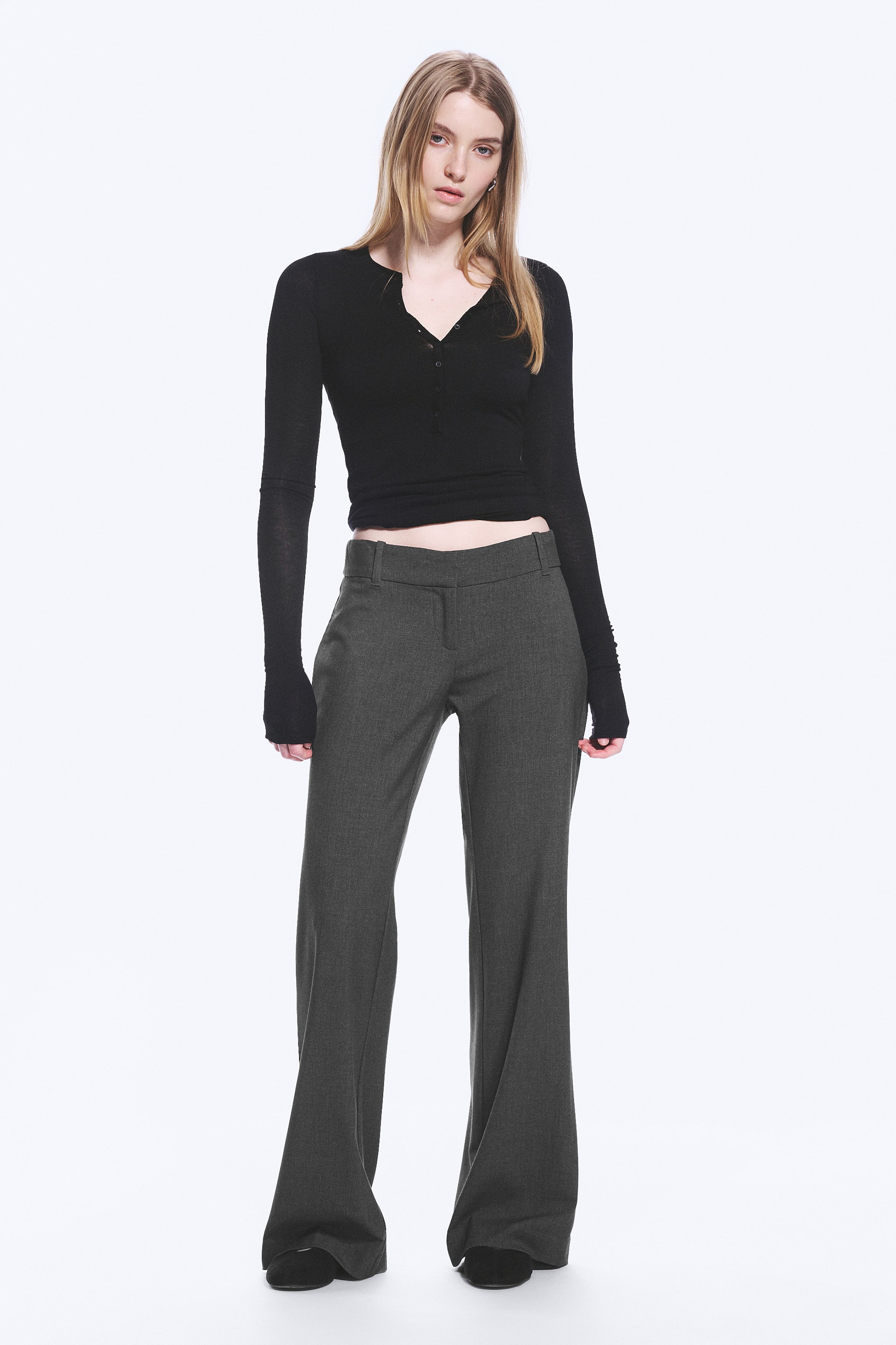 Vis større bilde: Mørkegrå bootcut-bukser med mellomhøy midje, beltehemper og skrå sidelommer. Buksene er rette gjennom låret og har en betydelig utsving fra kneet til falden.