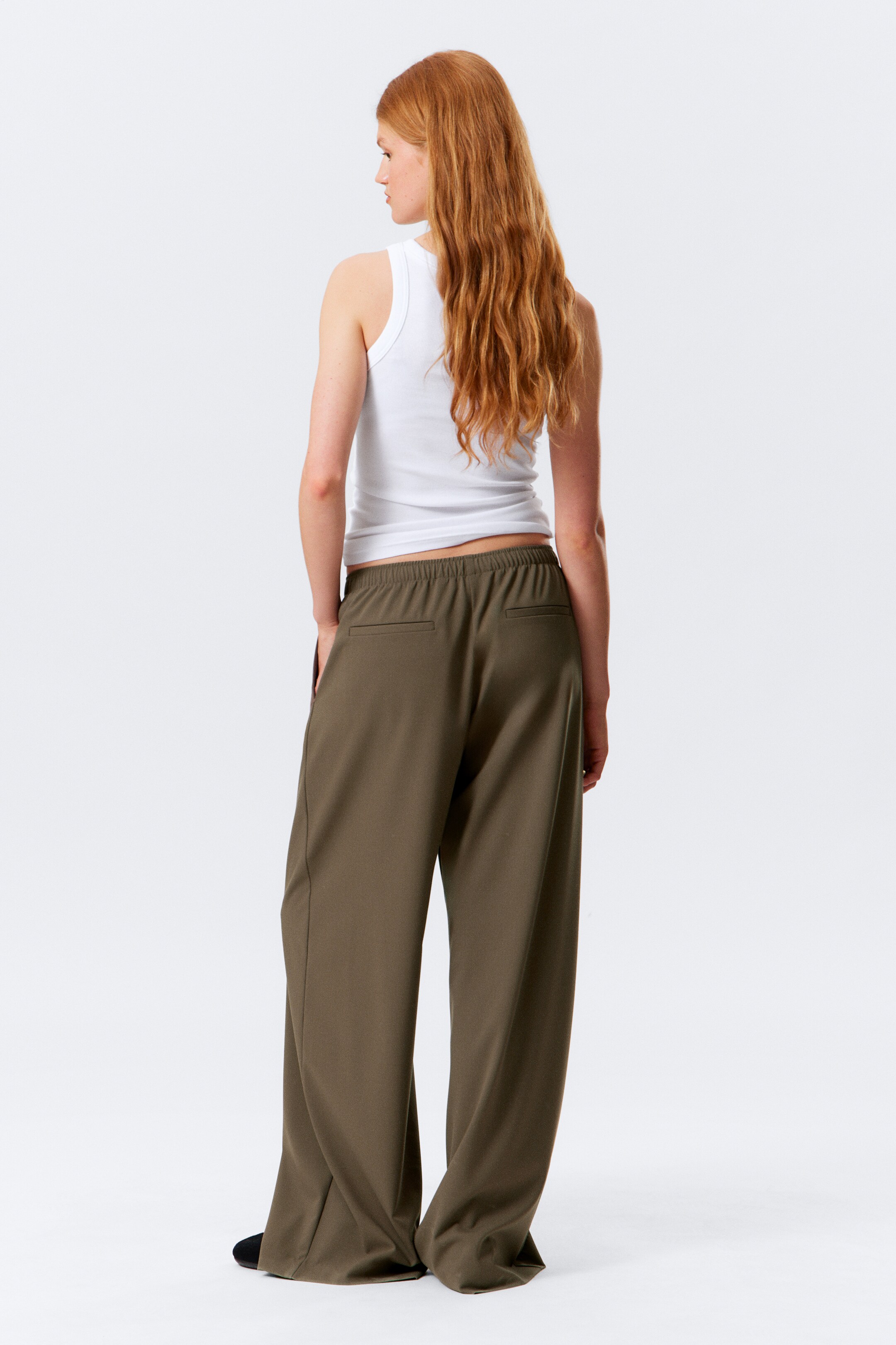 Visualizza immagine più grande: Pantaloni a gamba larga verde oliva, con cintura elasticizzata e due tasche posteriori a filetto, sono presentati da dietro. Una canotta bianca a coste è indossata sopra i pantaloni.