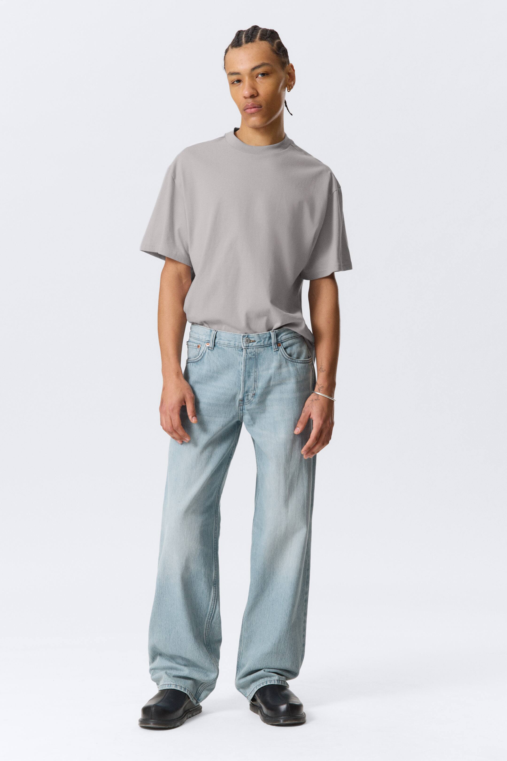 Agrandir l'image: Jean bleu clair, taille basse avec une coupe ample et droite, et une longueur généreuse, portés par le mannequin. Ces jeans présentent un design classique à 5 poches et une braguette à boutons, confectionnés en denim rigide en coton biologique enrichi de coton recyclé.