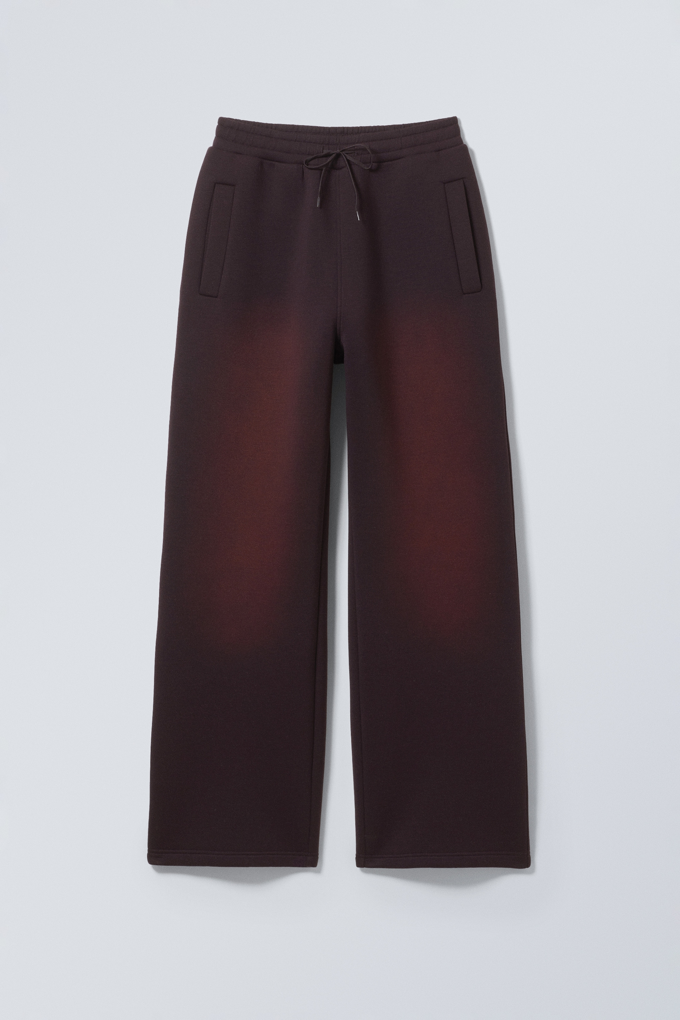 Agrandir l'image: Un pantalon de survêtement marron foncé à jambes larges est affiché en vue de face. Ils présentent un effet de dégradé brun rougeâtre sur le haut des cuisses, une taille élastique à cordon de serrage et deux poches frontales verticales.