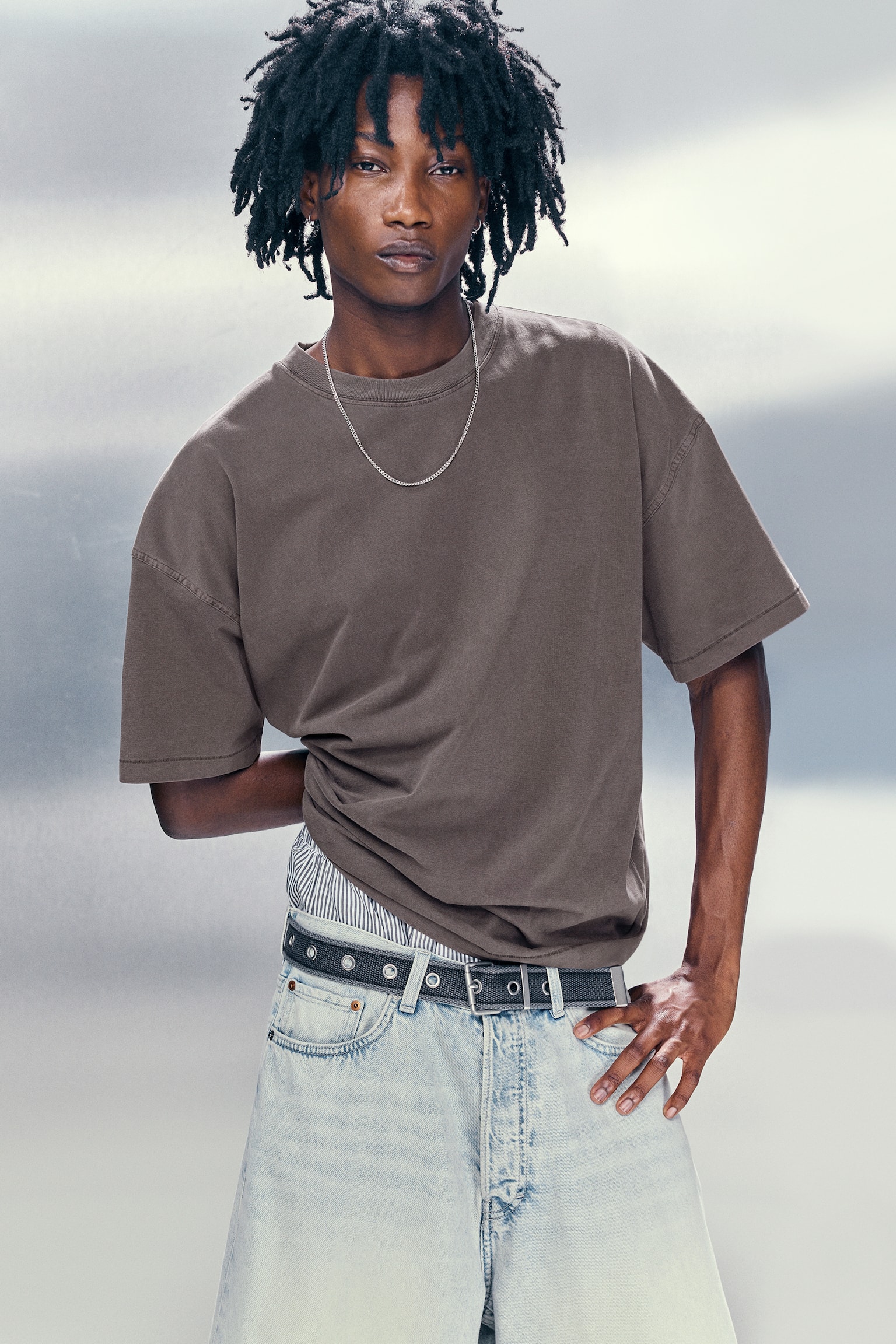 T-shirt ample et carré. Le t-shirt gris foncé délavé est présenté de face, avec un col rond côtelé et des manches courtes et larges avec des détails de couture visibles. Il affiche une coupe décontractée et carrée ainsi qu'un ourlet droit. - 1