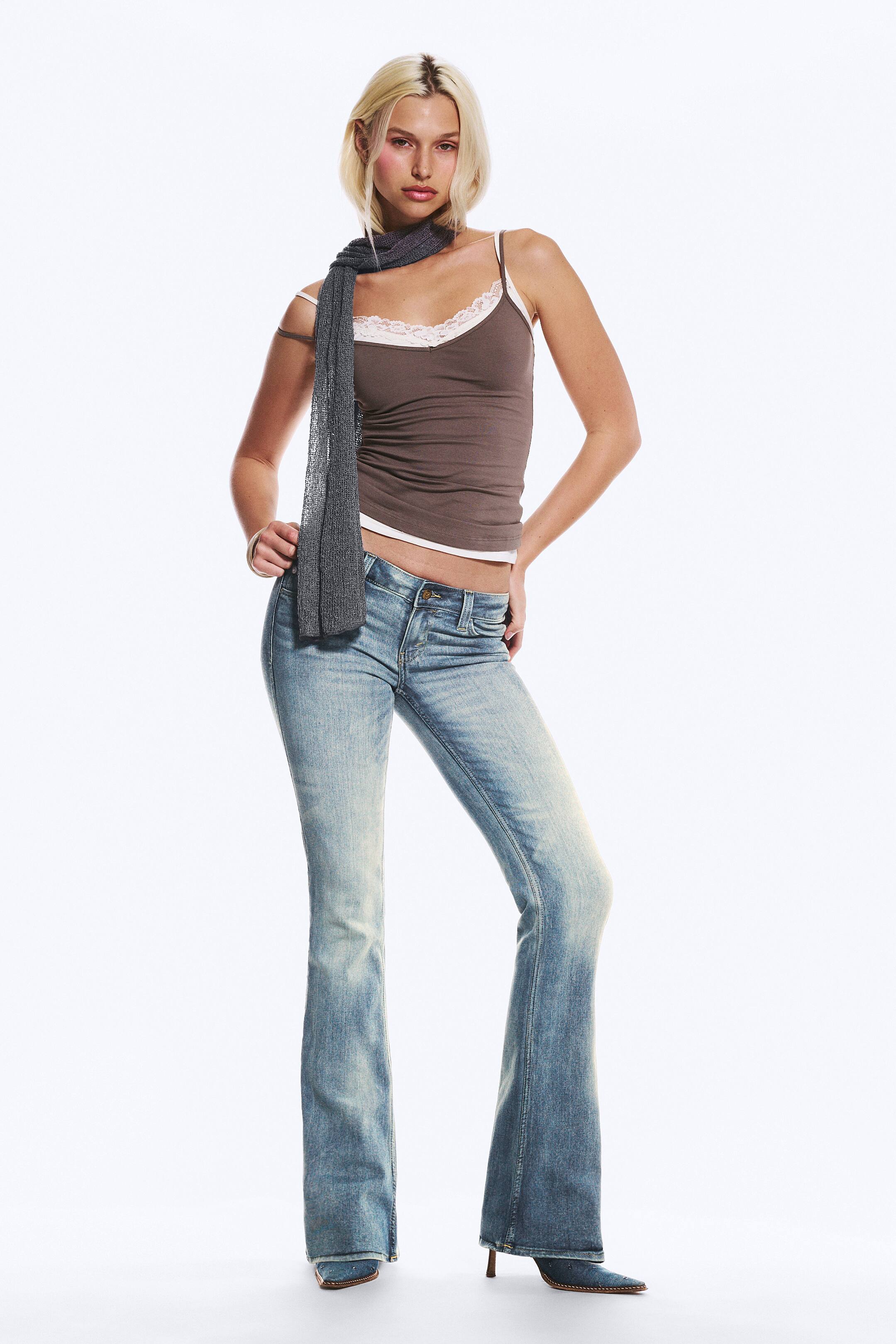 Visualizza immagine più grande: Una canottiera marrone è indossata, caratterizzata da sottili spalline bianche e uno scollo a V con bordo in pizzo bianco. Uno strato bianco è visibilmente sporgente dall'orlo inferiore e la canottiera aderisce strettamente al corpo.