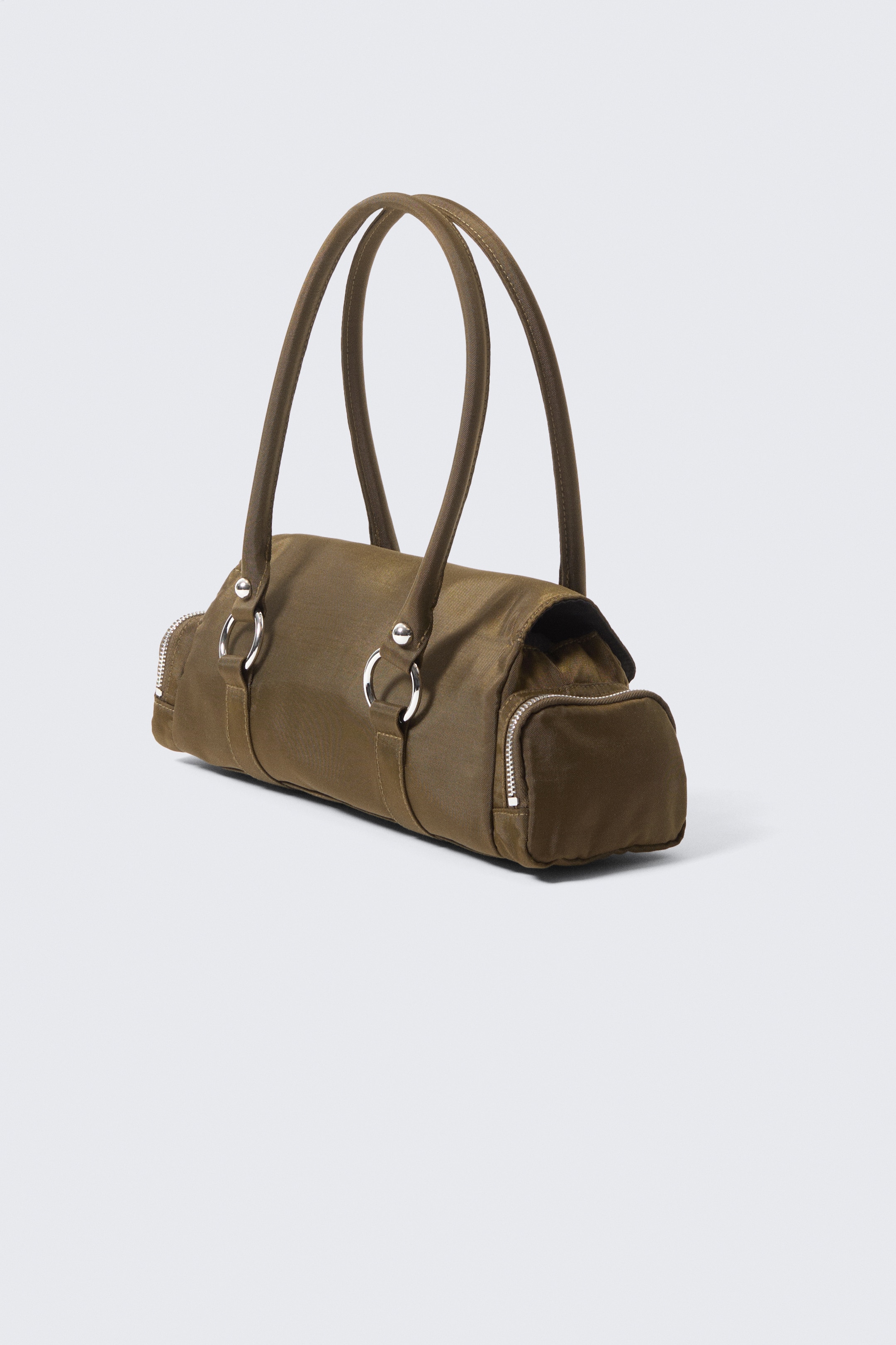 Grösseres Bild ansehen: Eine olivgrüne Handtasche im Duffel-Stil wird schräg präsentiert und verfügt über zwei obere Griffe, die durch silberfarbene Ringe verbunden sind. Reißverschlüsse sind an beiden Enden der Tasche sichtbar, und eine rechteckige Reißverschlusstasche befindet sich an der Seite.