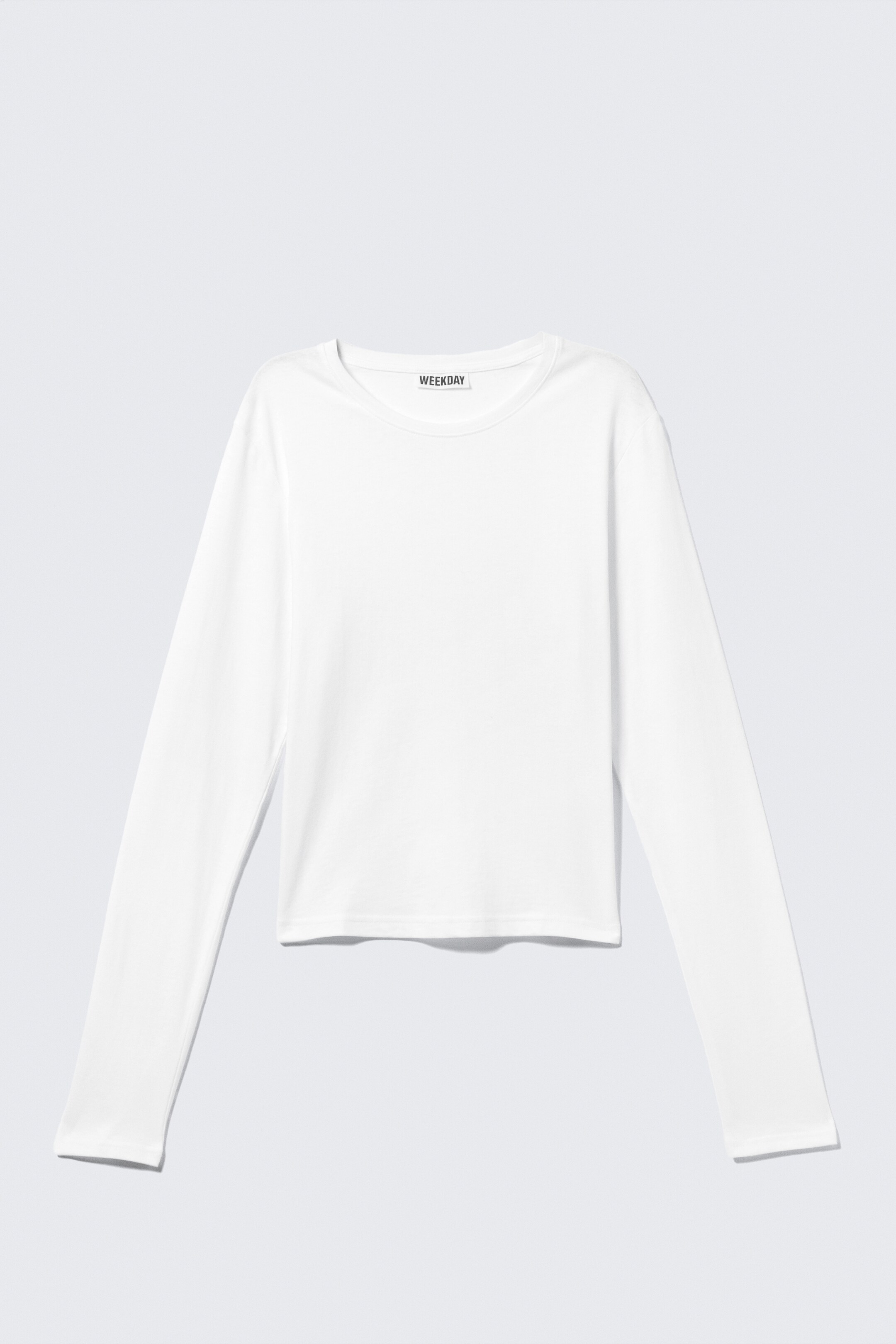 View larger image: A white long-sleeve top is displaying its FRONT, featuring a crew neck, long sleeves, and a straight hem. A black "WEEKDAY" label is visible on the inner collar.