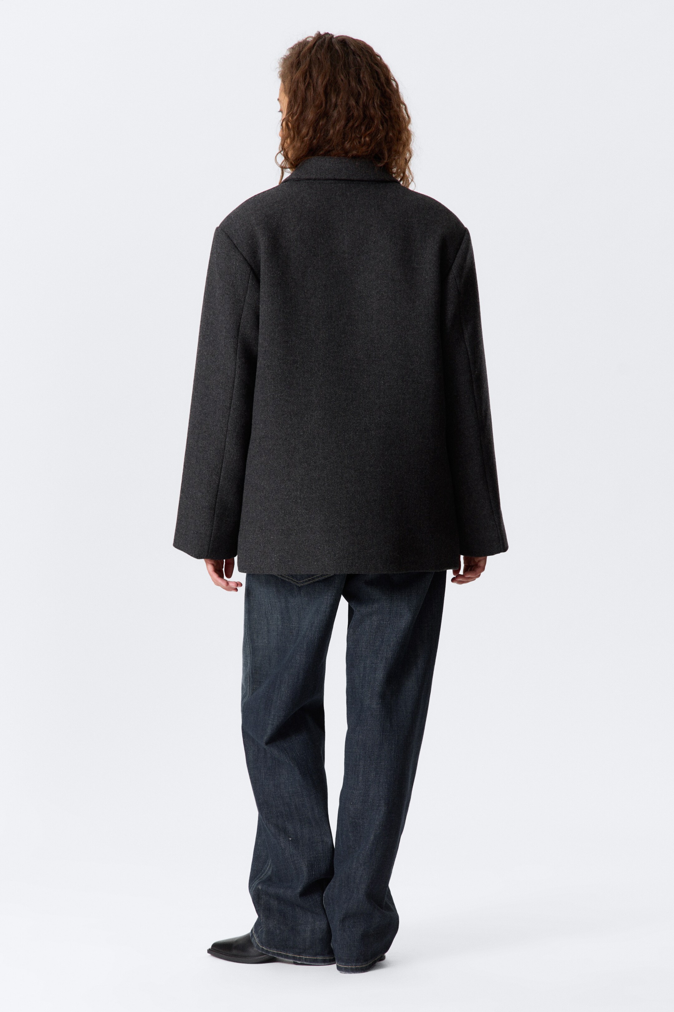 Größeres Bild ansehen: Eine dunkelgraue Jacke wird von hinten gezeigt, sie hat eine entspannte, kastenförmige Silhouette mit breiten, geraden Ärmeln und einem flachen Kragen und ist aus einem dunkelgrauen Webstoff gefertigt.