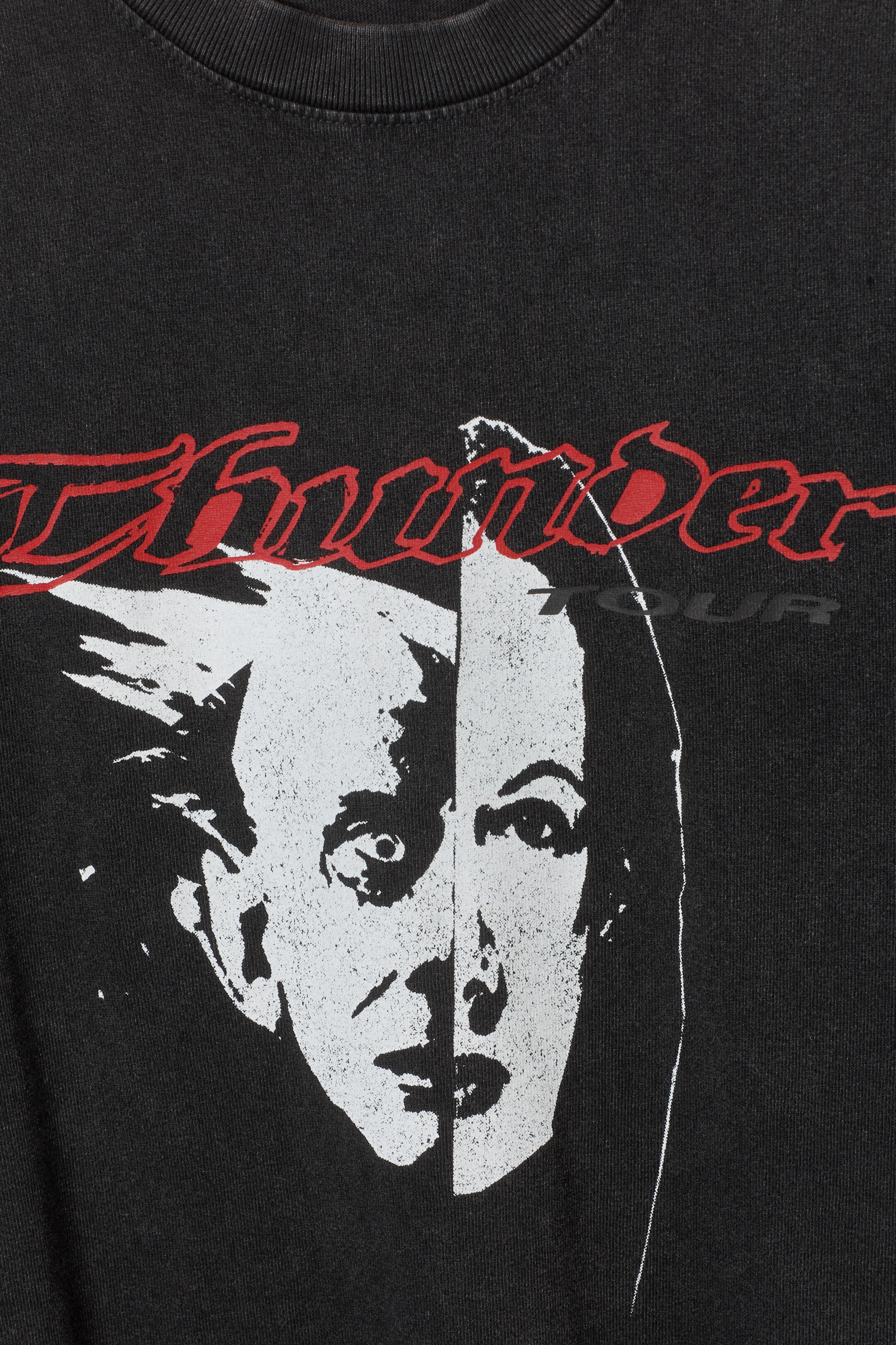 View larger image: A dark grey T-shirt is featuring a distressed graphic print on the FRONT, showcasing a white and light grey split-face design with red 'Thunder' text and smaller dark grey 'TOUR' text above it. It is designed with a ribbed crew neckline.