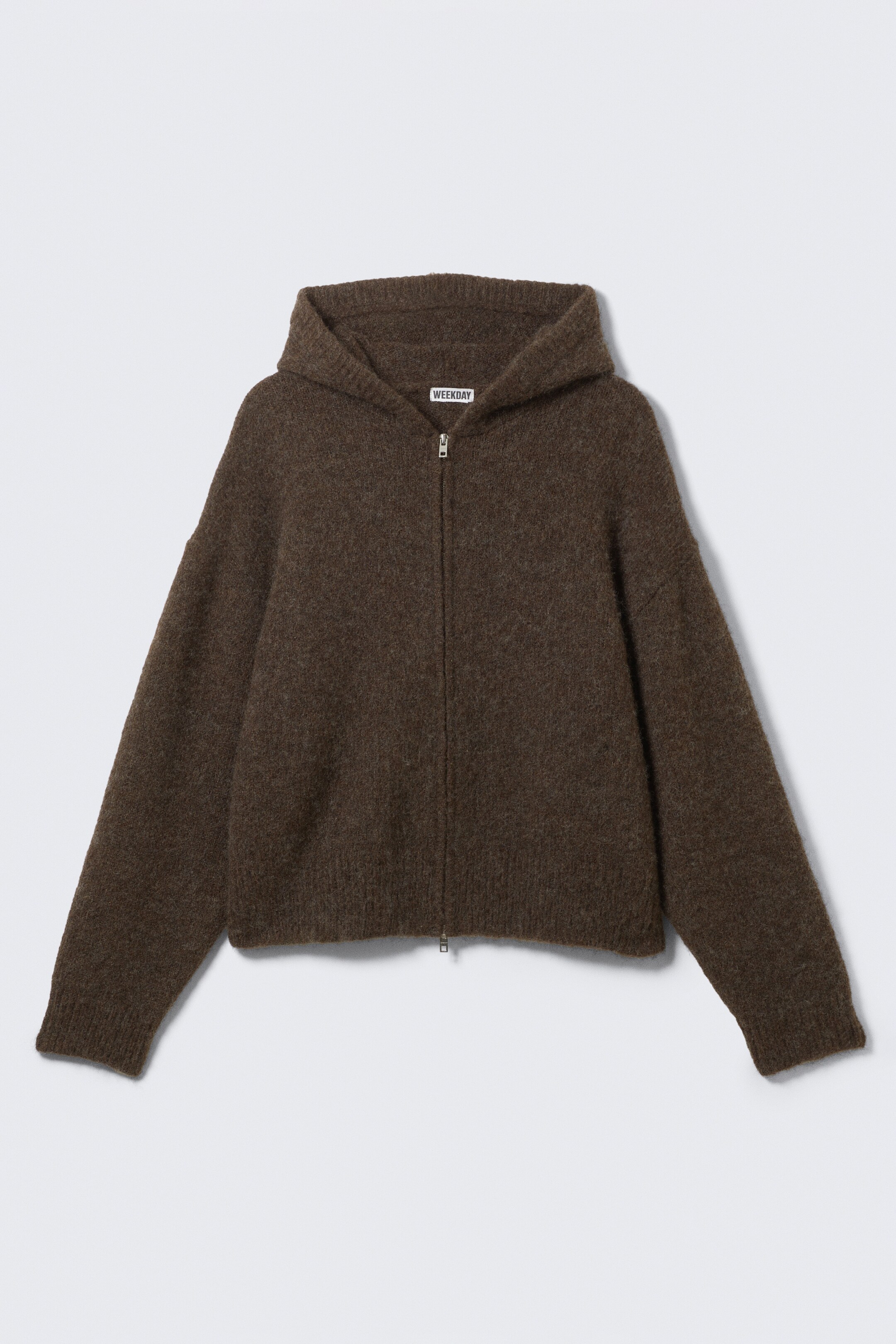 Visa större bild: En brun zip-up hoodie visar en lös, boxig passform från framsidan, med en mjuk, luddig textur. Den är designad med en dubbel-lager huva, tvåvägs dragkedja, ribbade muddar och fåll, samt en synlig vit 'WEEKDAY'-etikett på insidan av bakre halsringningen.
