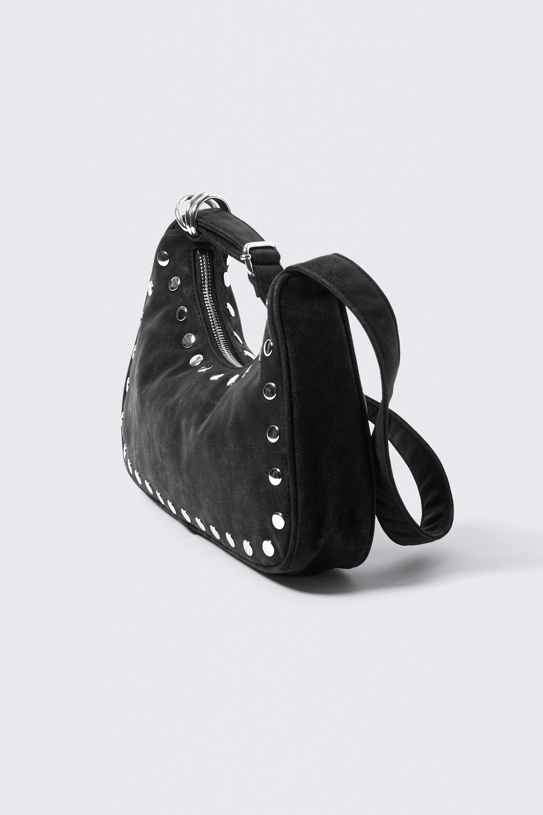 Ver imagen más grande: Un bolso de imitación de cuero negro cuenta con una silueta suave y esculpida, ricamente adornado con tachuelas en tono plateado en toda su superficie. Está diseñado con un cierre superior con cremallera en tono plateado y una correa ancha que se ajusta a través de un broche metálico.