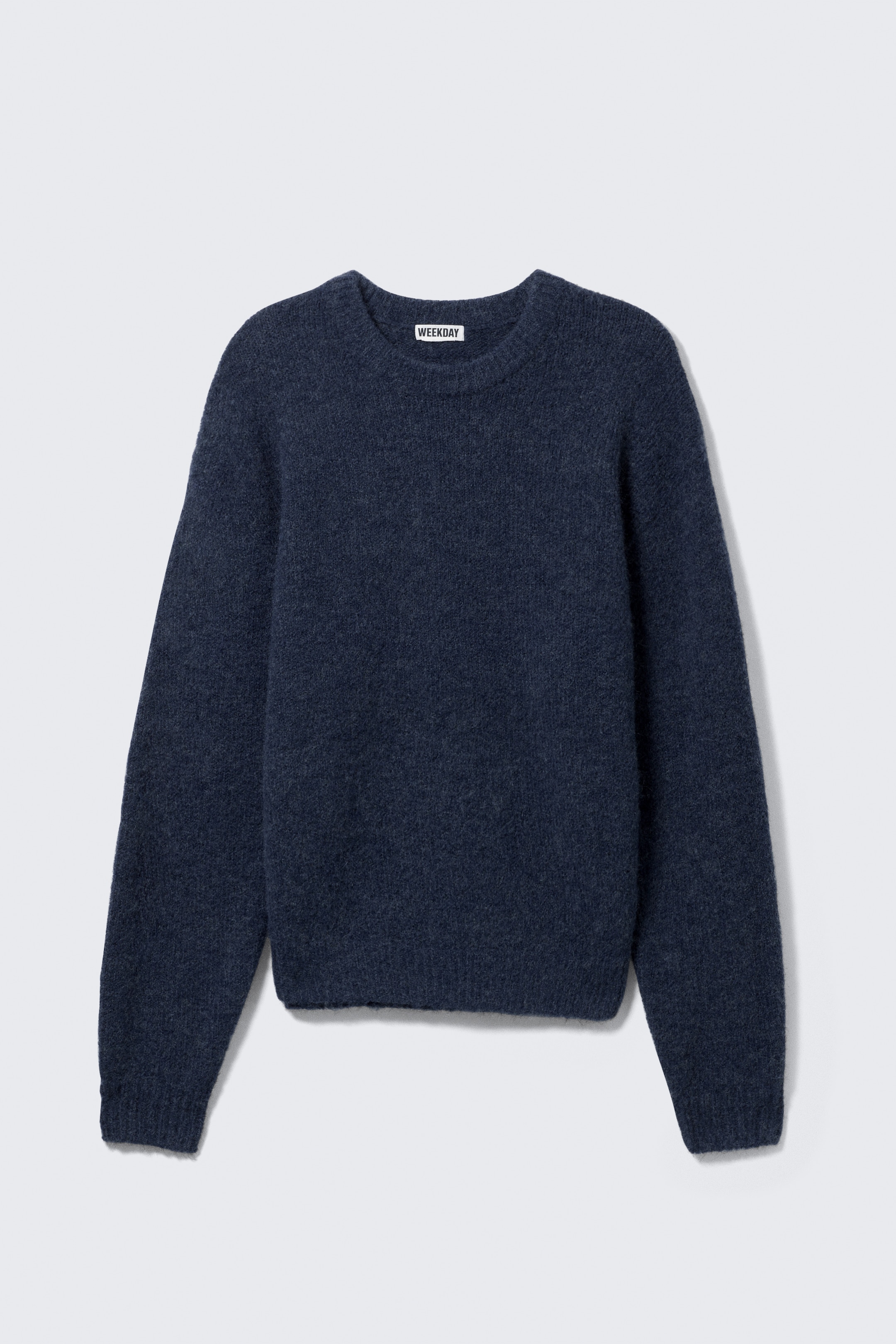 Ver imagen más grande: Un jersey de cuello redondo azul oscuro está extendido, de frente, mostrando una textura de punto suave y peluda. Se puede ver un sutil canalé en los puños y el dobladillo inferior, y una etiqueta blanca con la inscripción "WEEKDAY" se muestra en la parte posterior del cuello.