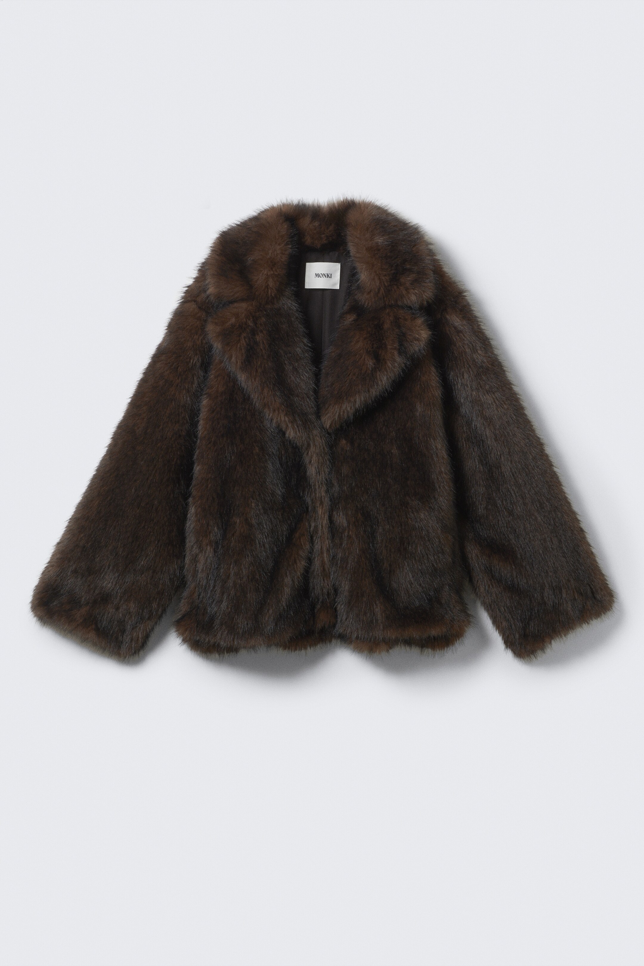 Agrandir l'image: Une veste en fausse fourrure marron foncé est présentée de face, avec un large col à revers crantés et des manches longues. Une étiquette de marque blanche "MONKI" est visible sur la doublure intérieure.