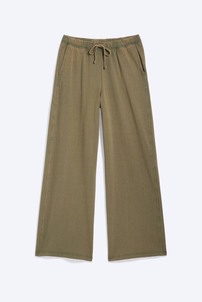 Eine olivgrÃ¼ne Loungehose wird von vorne gezeigt und prÃ¤sentiert eine entspannte, weit geschnittene Silhouette. Die Hose verfÃ¼gt Ã¼ber einen elastischen Bund mit einem farblich abgestimmten Kordelzug, der mittig gebunden ist, sowie seitliche SchrÃ¤gtaschen. - 1