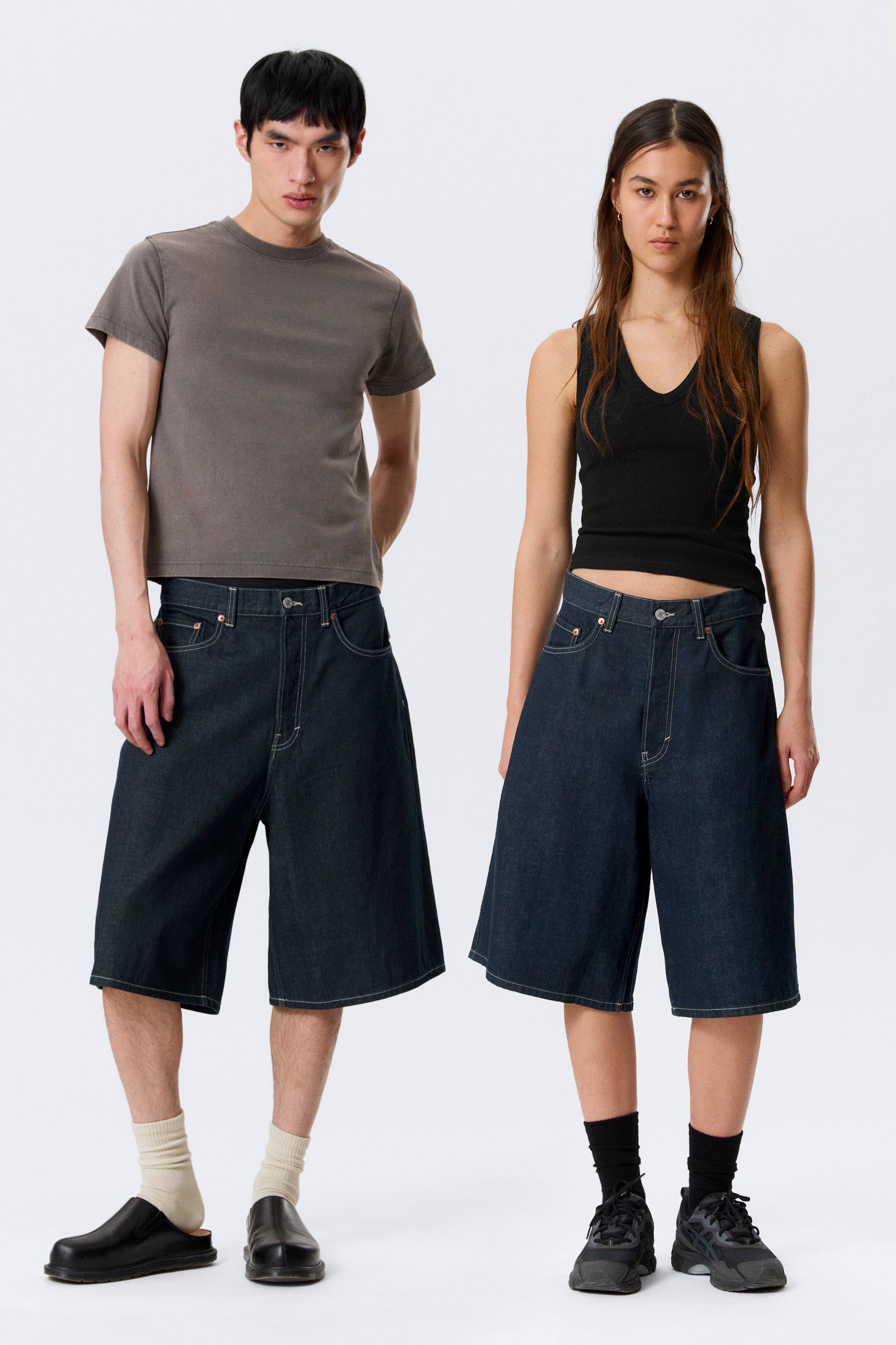 Grösseres Bild ansehen: Dunkel gewaschene Denim-Culottes mit einem weiten Bein, das bis zur Mitte der Wade fällt. Sie präsentieren einen hochgeschnittenen Sitz mit kontrastierenden hellen Nähten, die an den Vorder- und Rückentaschen, Nähten und dem Knopfverschluss sichtbar sind.