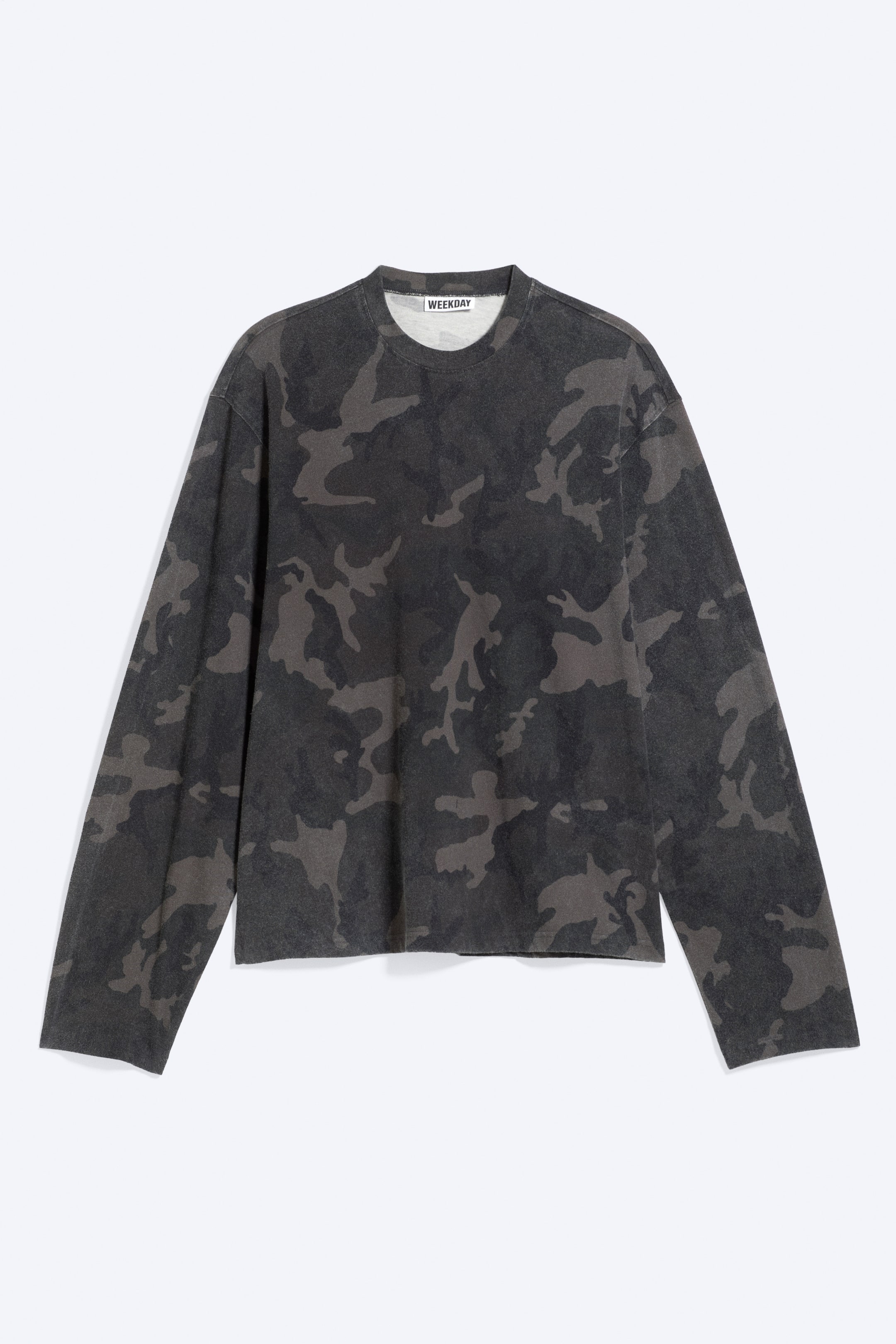 Größeres Bild anzeigen: Ein Langarm-T-Shirt liegt flach und nach vorne ausgerichtet und zeigt ein verwaschenes dunkles Camouflage-Muster in Grau- und Schwarztönen. Es ist mit Rundhalsausschnitt, schlichten Bündchen und geradem Saum gestaltet, während im Nackenbereich ein „Weekday“-Label sichtbar ist.
