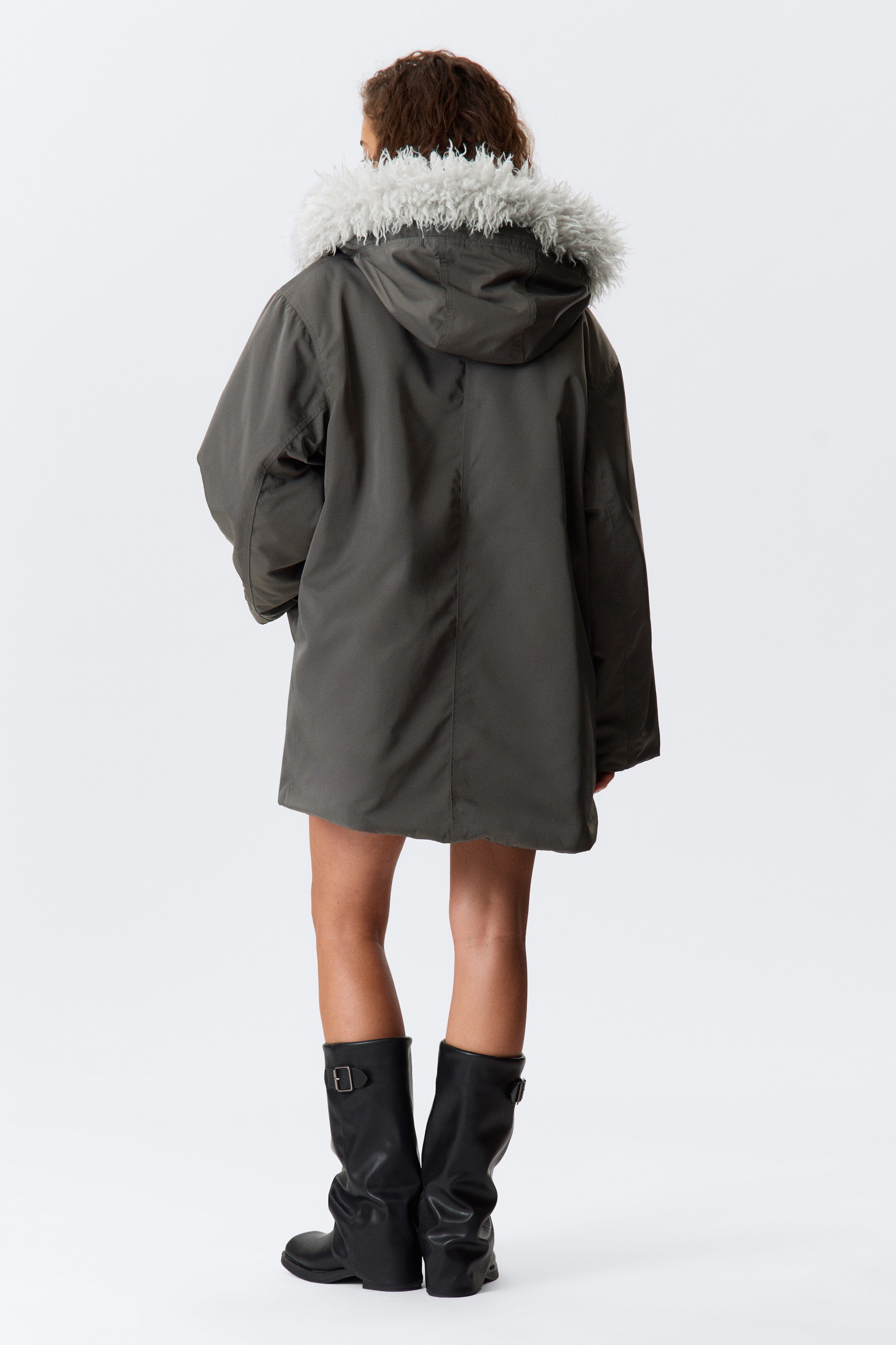 Grotere afbeelding bekijken: Een donkergroene parka wordt van de achterkant getoond, met een capuchon met een ruige lichtgrijze faux bont rand. De parka is ontworpen met een relaxte pasvorm en reikt tot halverwege de dijen.