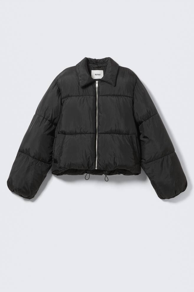 A black puffer jacket is presenting a cropped, voluminous FRONT silhouette, featuring a full-length silver-toned zipper and a pointed collar. Horizontal baffles are creating a puffy design across the body and sleeves, with the hem cinched by visible drawstrings and toggles. - 1