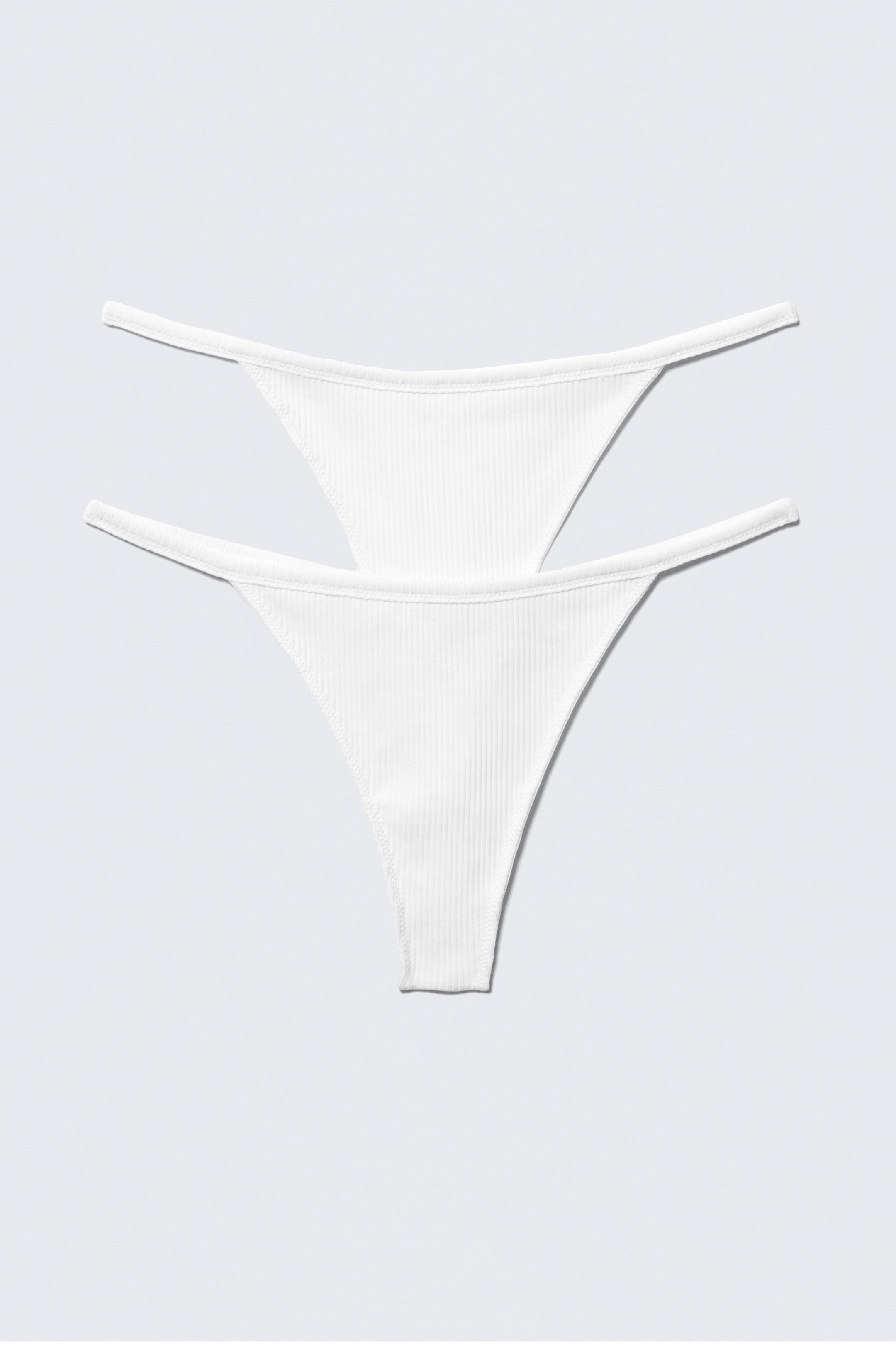 Visa större bild: Två vita ribbade stringtrosor visar sina V-formade framstycken och tunna sidoband.