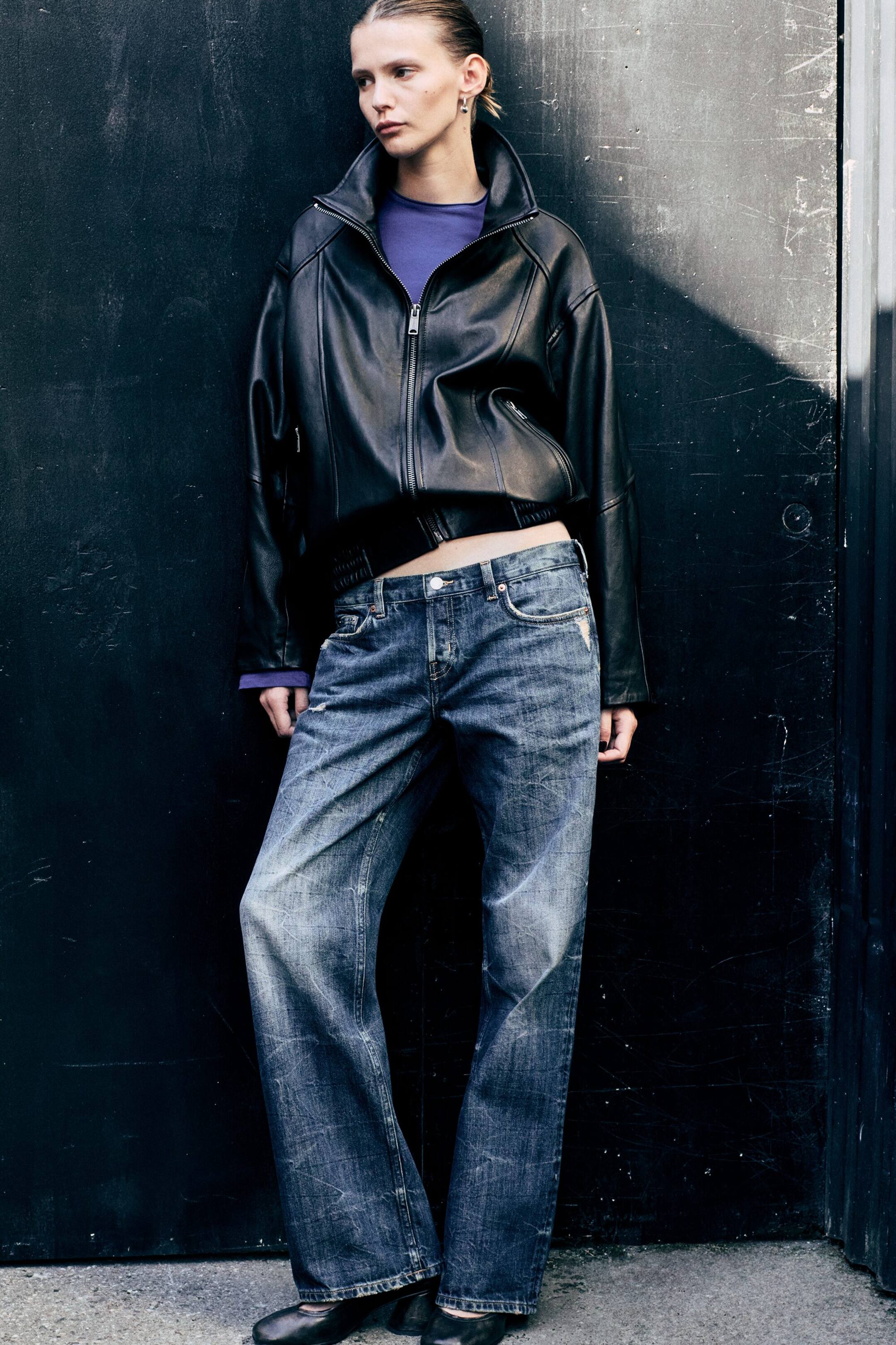 Visa större bild: Jeans med låg midja tillverkade av blekt blå denim bärs av modellen och har en avslappnad passform samt en diskret bootcut-benvidd. Jeansen stylas med en svart läderjacka med dragkedja och en lila topp.