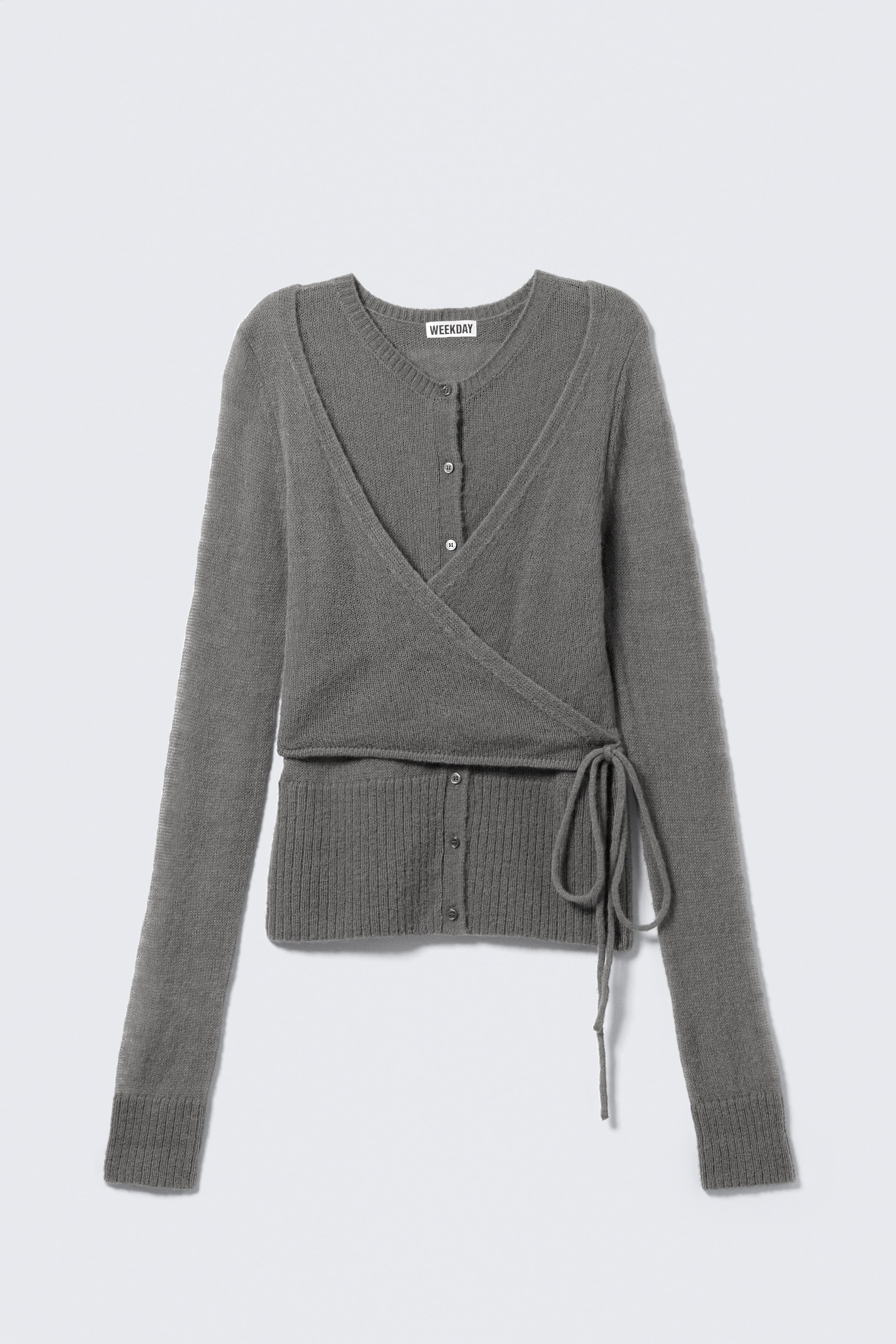 Agrandir l'image: Un cardigan en tricot gris est présenté de FACE, avec un design en couches. Un cardigan à col rond boutonné est visible sous une partie extérieure croisée à l'avant et nouée à la hanche gauche, les deux sections affichant des manches longues, des poignets côtelés et des ourlets côtelés.