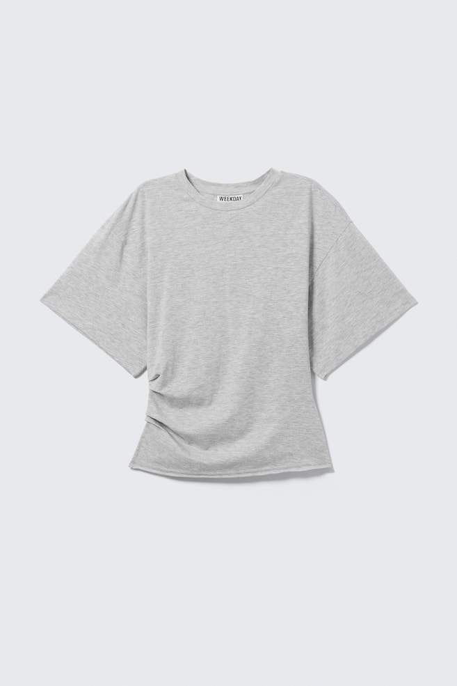 Jasnoszary T-shirt pokazany jest z przodu, z szerokimi, pudeÅkowatymi rÄkawami i klasycznym okrÄ
gÅym dekoltem. Ubranie prezentuje marszczonÄ
, drapowanÄ
konstrukcjÄ z umieszczonymi zakÅadkami po jednej stronie talii oraz surowo wykoÅczonym doÅem. - 1