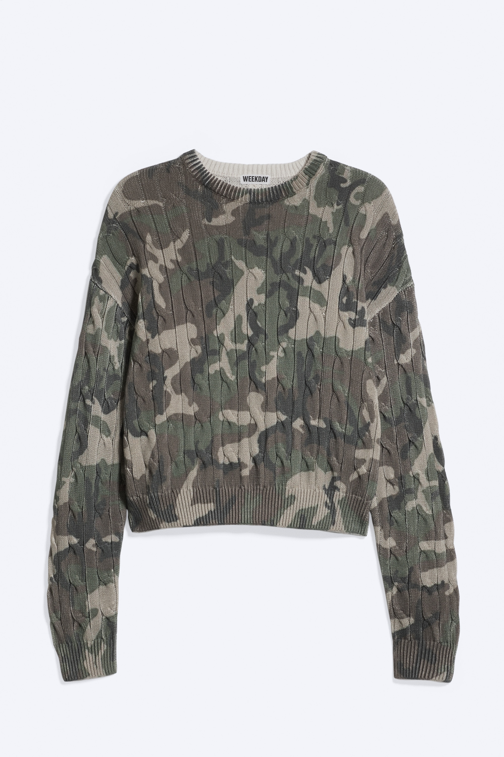 Rennon istuva kaapelineulottu camo-kuosinen neulepaita on mallin yllä. Siinä on pyöreä pääntie, laskettu olkalinja ja ribbiresorit. Neulepaita on stailattu mustalla neuloksisella huivilla, joka on kerroksittain kaulan ympärillä, sekä mustalla olkahihnalla, joka kulkee vinosti rinnan yli.