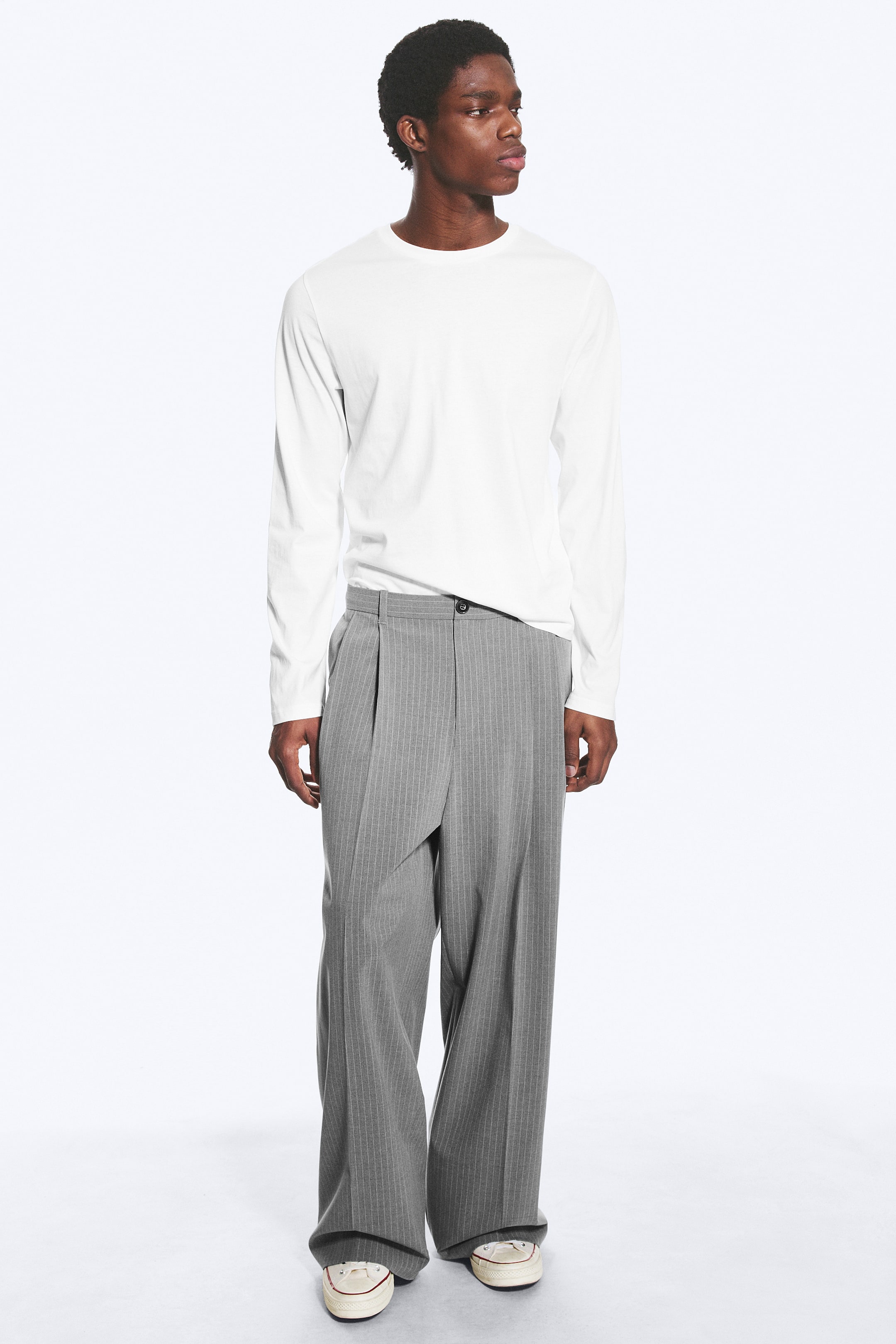 Agrandir l'image: Pantalons à rayures grises sont conçus avec une coupe ample et une silhouette taille haute, dotés de plis profonds simples. Ils présentent une fermeture frontale superposée avec un bouton noir visible, s'étendant sur toute la longueur pour recouvrir les chaussures.