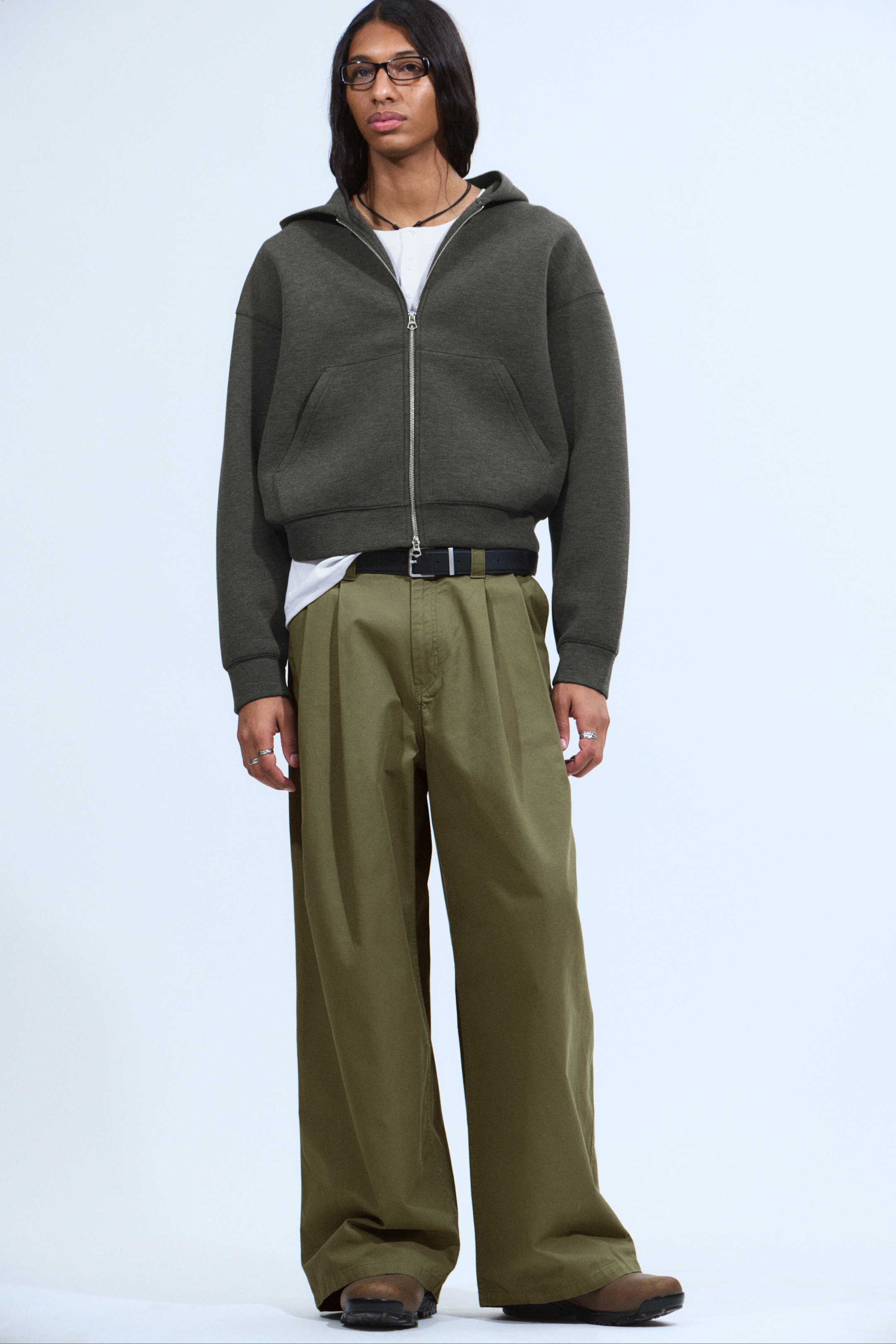 Visualizza immagine più grande: Una felpa con cappuccio con zip di colore verde oliva scuro e vestibilità regolare viene presentata FRONTE, realizzata in un tessuto scuba spesso. Presenta spalle leggermente cadenti, polsini e orlo a coste, grandi tasche frontali e una robusta cerniera frontale a due vie.