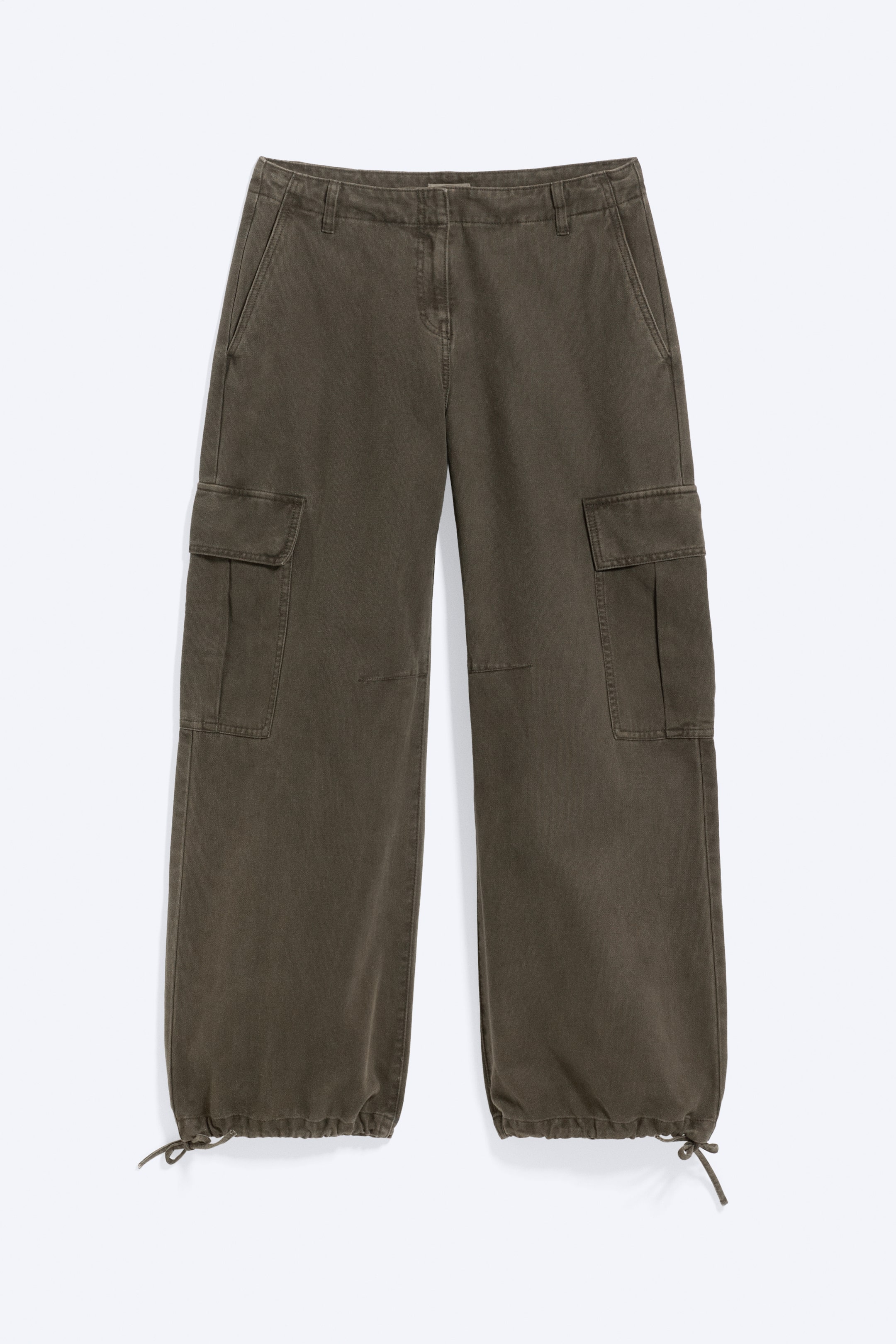 Grösseres Bild ansehen: Eine dunkelolivfarbene Cargo-Hose ist von vorne zu sehen und zeichnet sich durch eine lockere, weit geschnittene Passform mit schrägen Seitentaschen sowie grossen Cargo-Taschen mit Patte an den Beinseiten aus. Die Hose verfügt über einen Knopf- und Reissverschluss sowie verstellbare Saumzugbänder, die unten gerafft und gebunden sind.