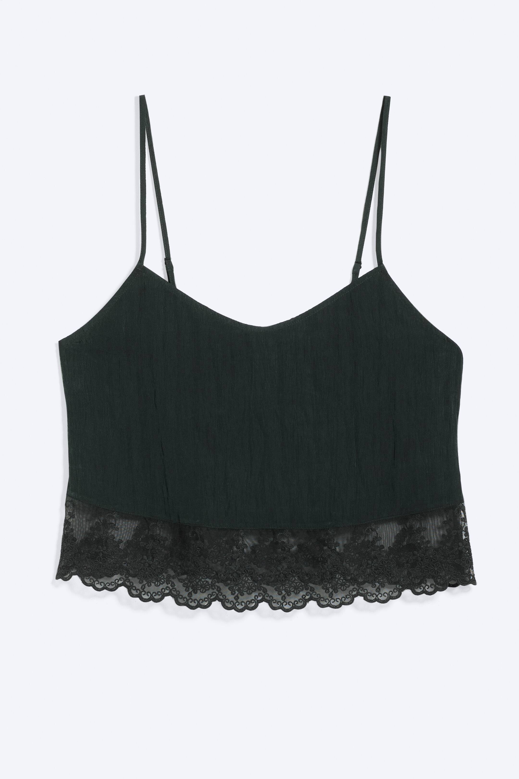 Grotere afbeelding bekijken: Een cropped camisole met kanten afwerking is aan de voorkant te zien, met dunne verstelbare spaghettibandjes en een V-hals. De donkergekleurde camisole heeft een getextureerde stof en een zwarte bloemenkant met een geschulpte rand langs de onderzoom.