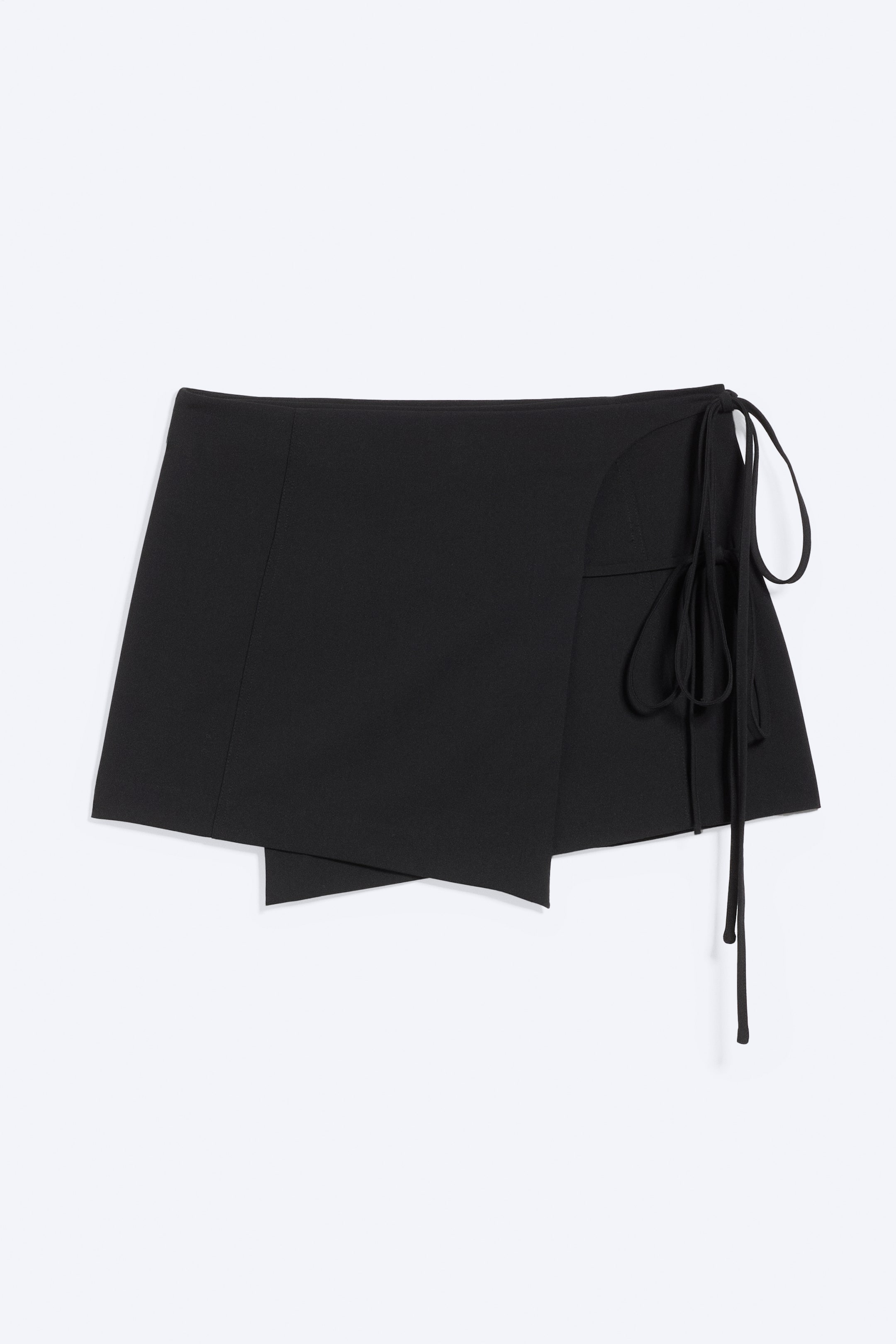Agrandir l'image: Une jupe portefeuille noire est présentée de face, avec un ourlet asymétrique et des liens réglables sur le côté droit. Elle est conçue avec des panneaux superposés et une ceinture lisse et épurée.