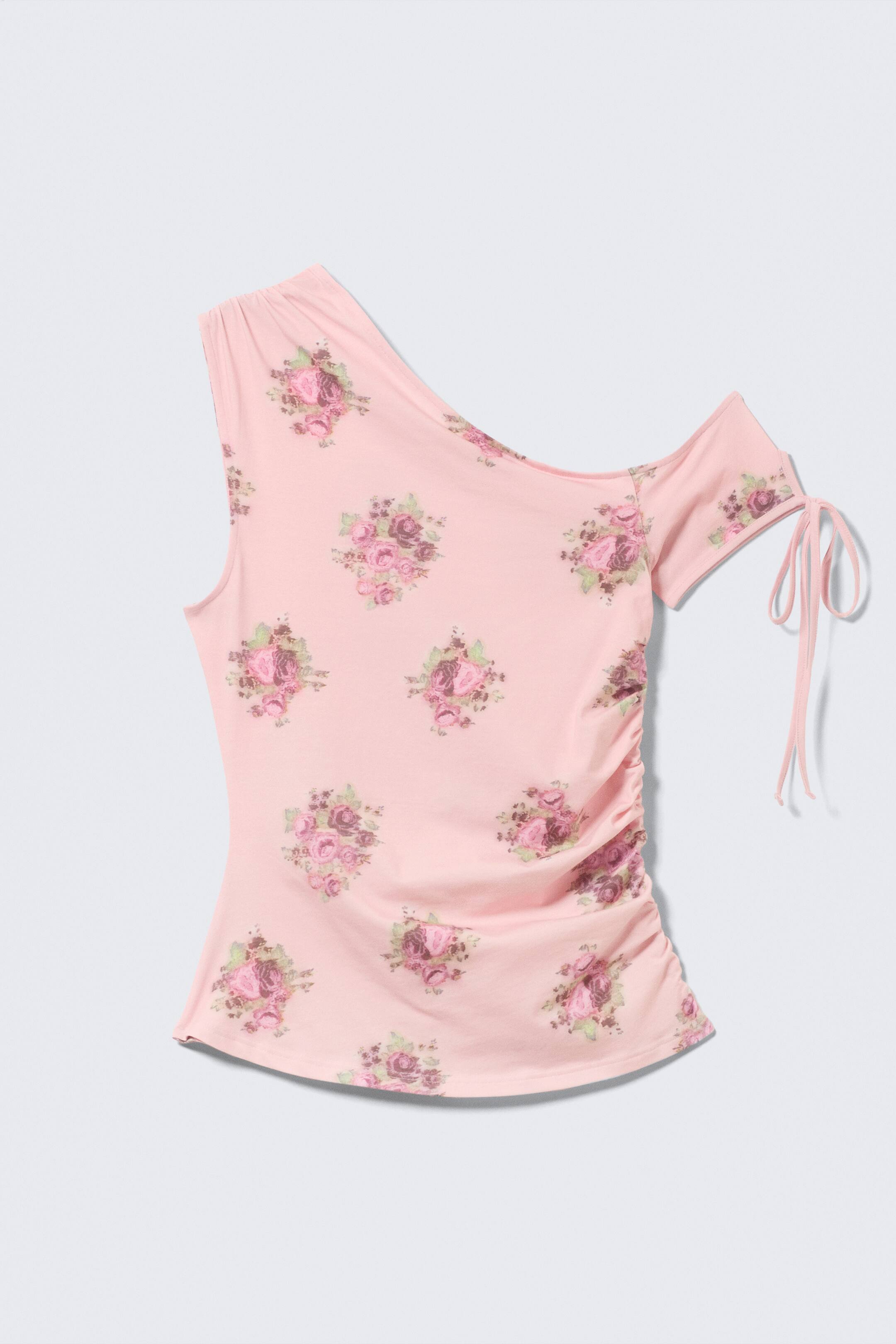 Ver imagen más grande: Un top floral rosa de un solo hombro se presenta desde el frente, con una base rosa claro adornada con patrones de rosas dispersas en tonos de rosa y verde. Está diseñado con un hombro izquierdo sin mangas, una manga derecha caída con detalles de lazo y fruncido a lo largo de la costura lateral derecha.