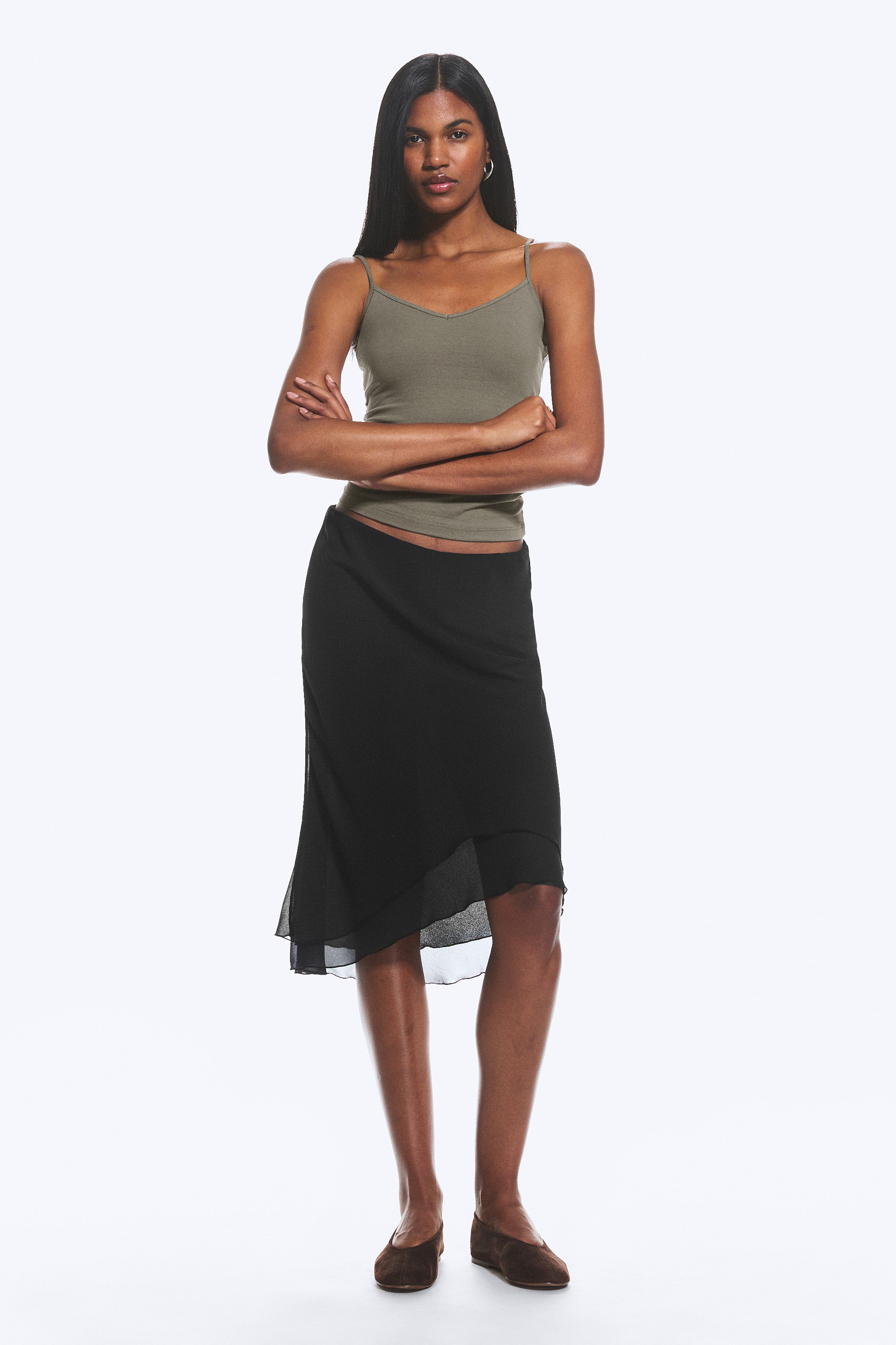 View larger image: A black midi skirt featuring an opaque base with a sheer, asymmetrical overlay, creating a layered effect. The skirt gracefully falls to mid-calf, presenting a flowing silhouette.