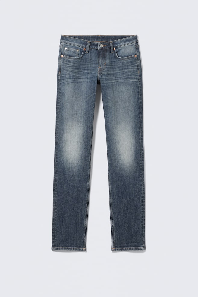Et par blå denimjeans vender FRONT, og viser en medium vask med lysere falmning på lårene og diskrete "whiskers". De har en linning med bæltestropper, en knaplukning, en lynlåsgylp og en femlommet stil med synlige metalnitter. - 1