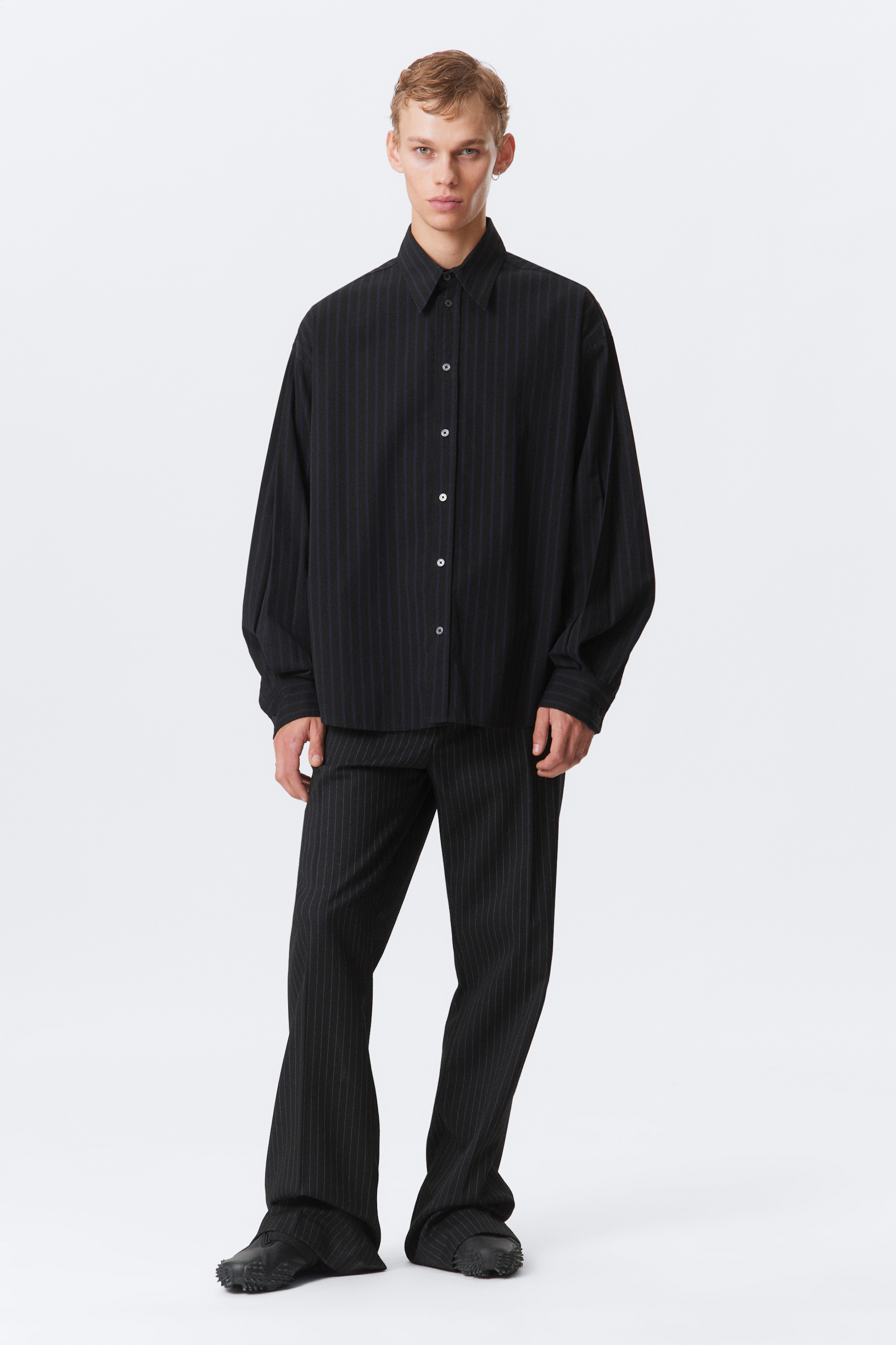 Ver imagen más grande: Una camisa negra de rayas finas de manga larga y unos pantalones anchos a juego se están mostrando, mirando hacia adelante. La camisa holgada presenta un cuello y botones blancos, mientras que los pantalones de ajuste suelto tienen un corte de largo completo.