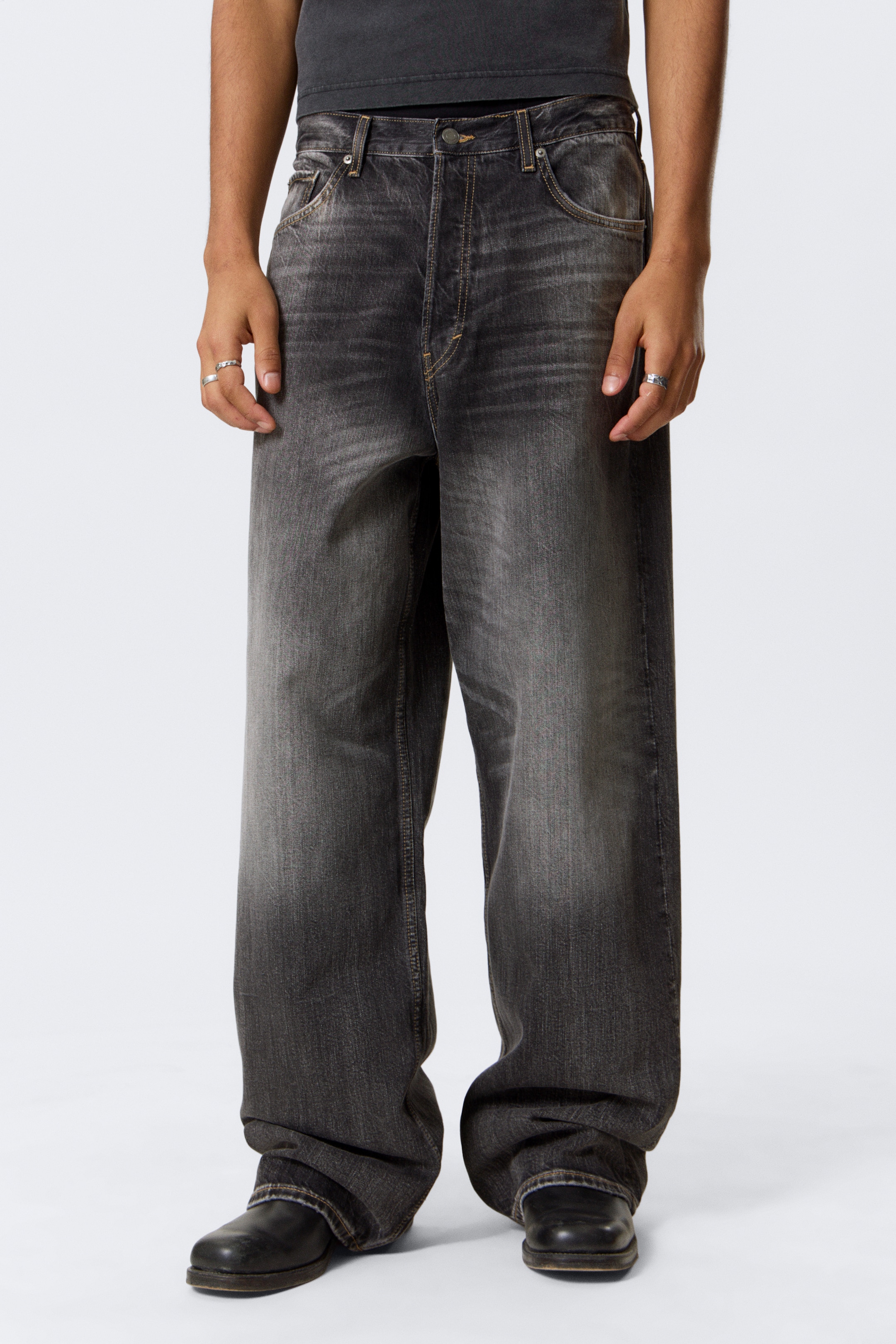 Ingrandisci l'immagine: Jeans grigio scuro a vestibilità ampia sono mostrati dal davanti, caratterizzati da un lavaggio usurato con sbiaditure più chiare sulle cosce e un taglio a gamba larga che si accumula alle caviglie. Sono progettati con uno stile a cinque tasche, una patta con bottoni visibili e cuciture a contrasto.