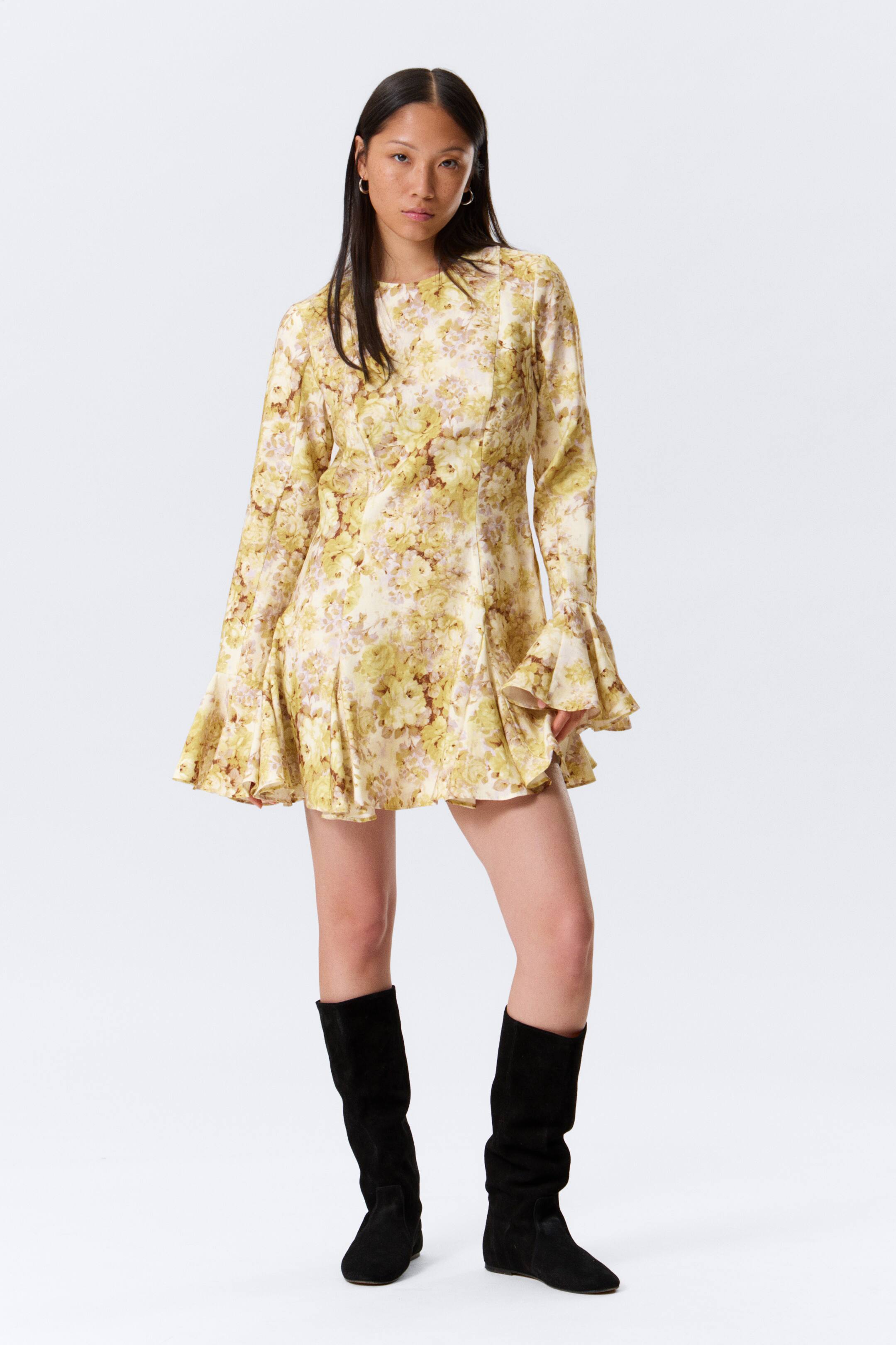 Größeres Bild anzeigen: Ein gelbes Minikleid mit Blumenmuster präsentiert sich mit einem runden Ausschnitt, einem eng anliegenden Oberteil, langen Ärmeln mit Glockenmanschetten und einem ausgestellten Rock, nach vorne gerichtet.